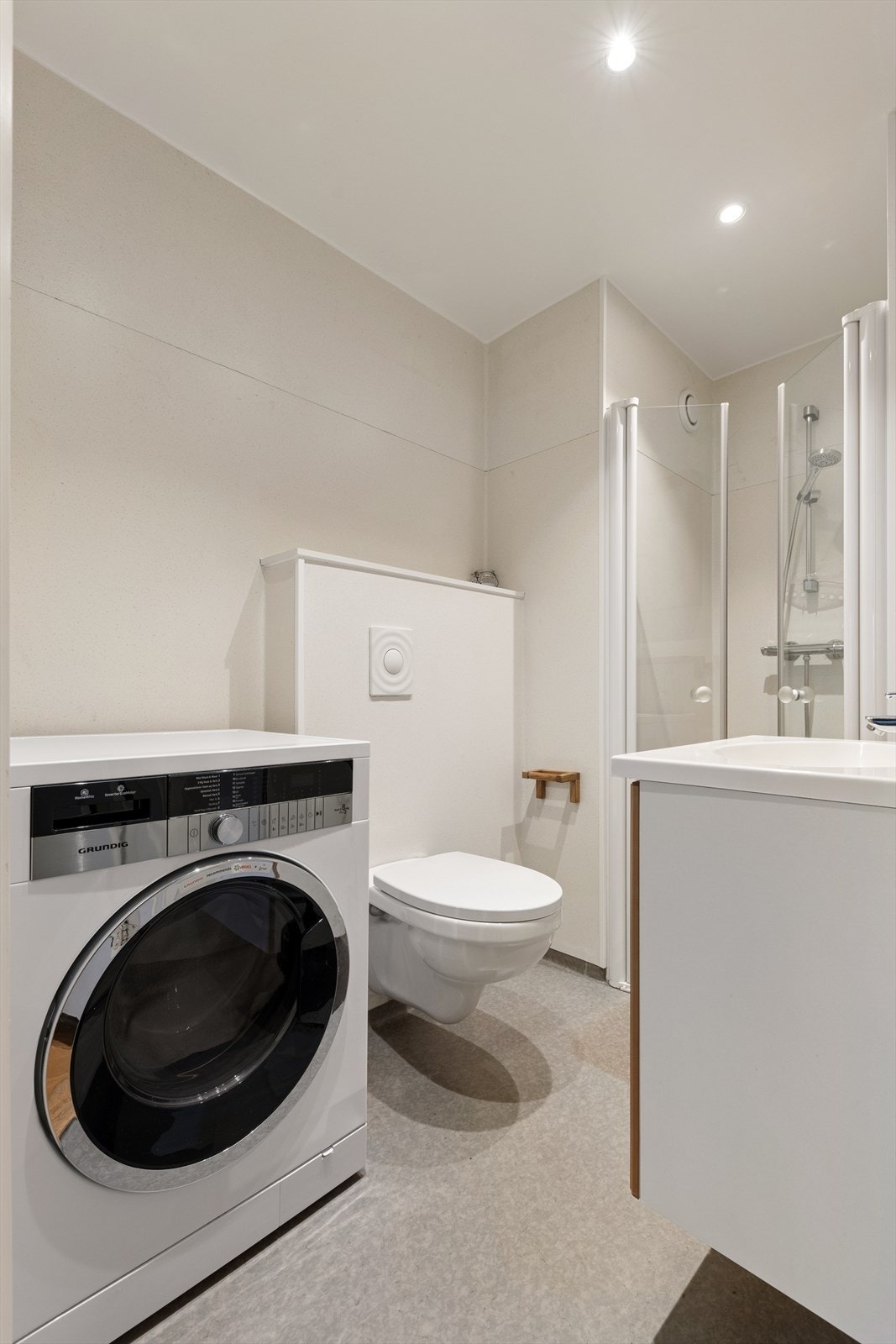 Funksjonelt lyst bad med vegghengt toalett, dusjnisje og opplegg for vaskemaskin Galleribilde
