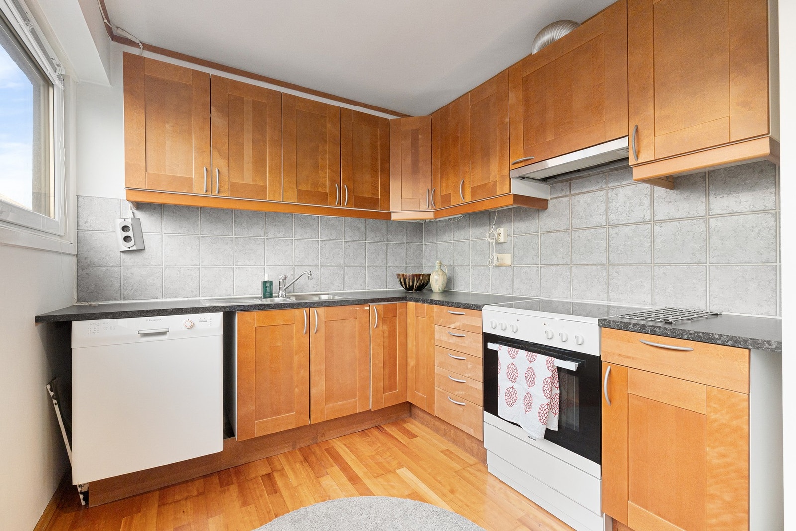 Eldre kjøkkeninnredning med slette fronter, fliser og enkel belysning over laminat benkeplate. Galleribilde