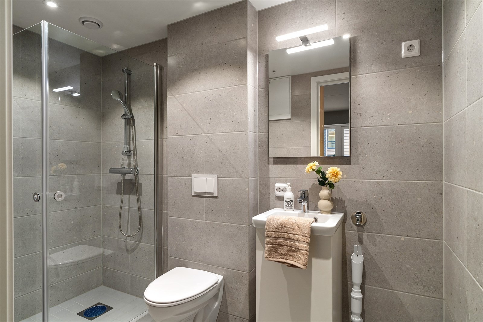 Flott helfliset bad, innredet med vegghengt wc, liten seksjon med vask og dusjhjørne. Opplegg for vaskemaskin Galleribilde