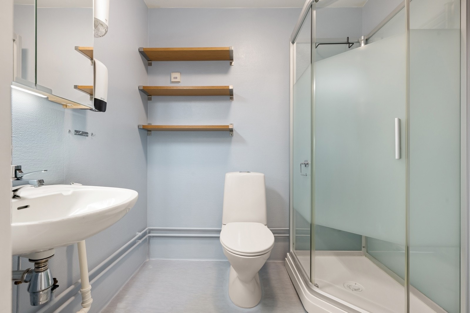 Badet er bestående av servant, veggskap med speilfronter, dusjkabinett, gulvmontert klosett og opplegg for vaskemaskin. Galleribilde