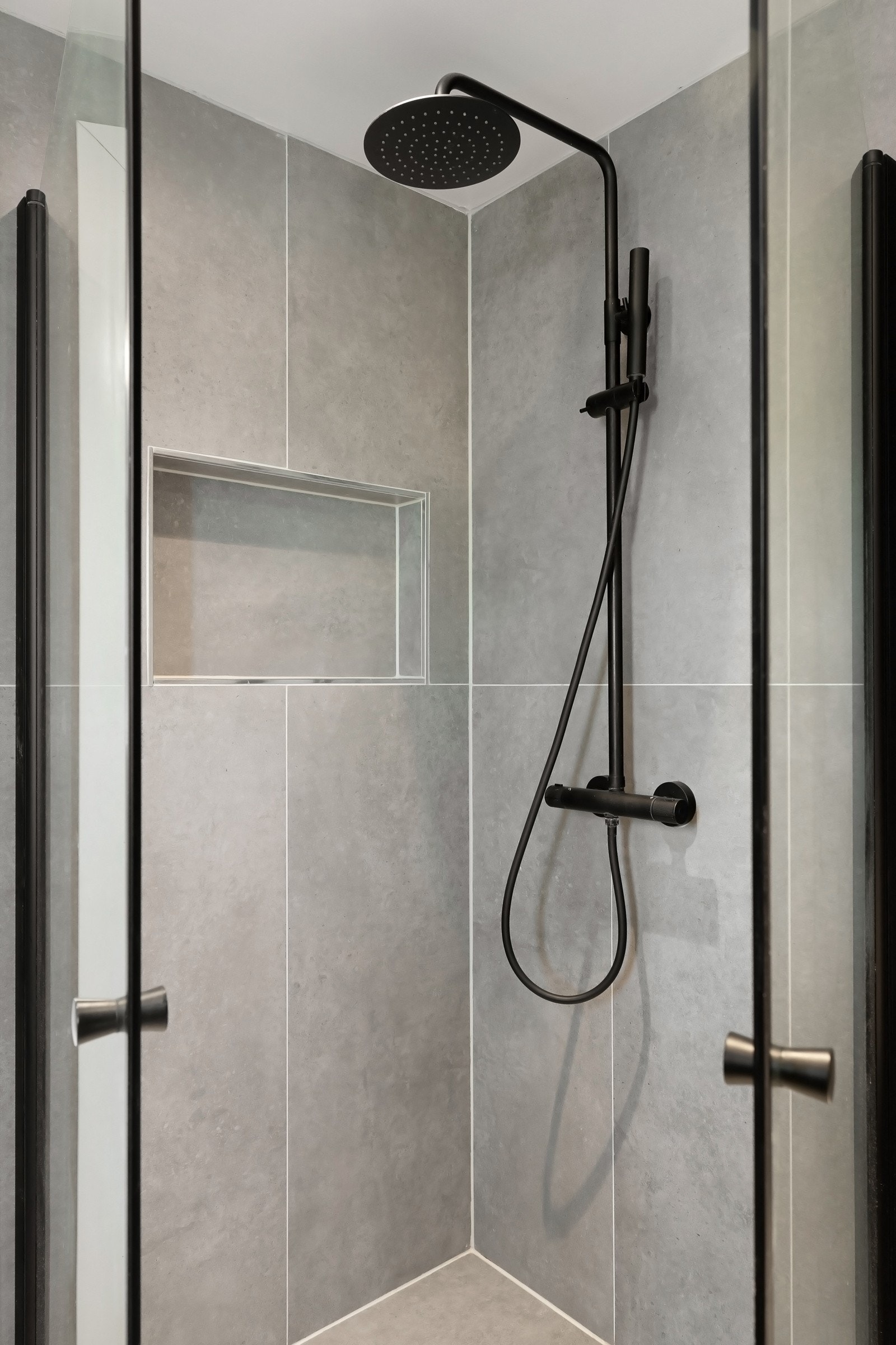 Romslig dusjnisje med sorte detaljer og innfelt dusjhylle i vegg. Galleribilde
