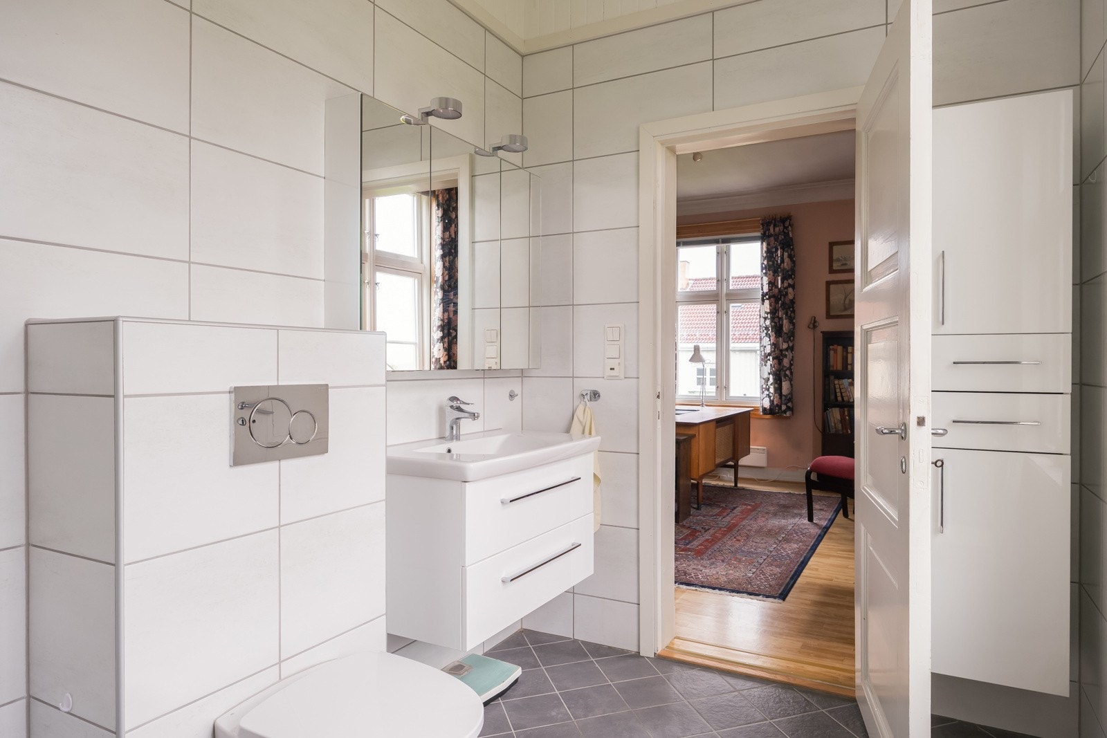 Rommet er utstyrt med flislagte overflater, gulvvarme, lagringsrike baderomsmøbler, servant, dusjhjørne og vegghengt toalett. Galleribilde