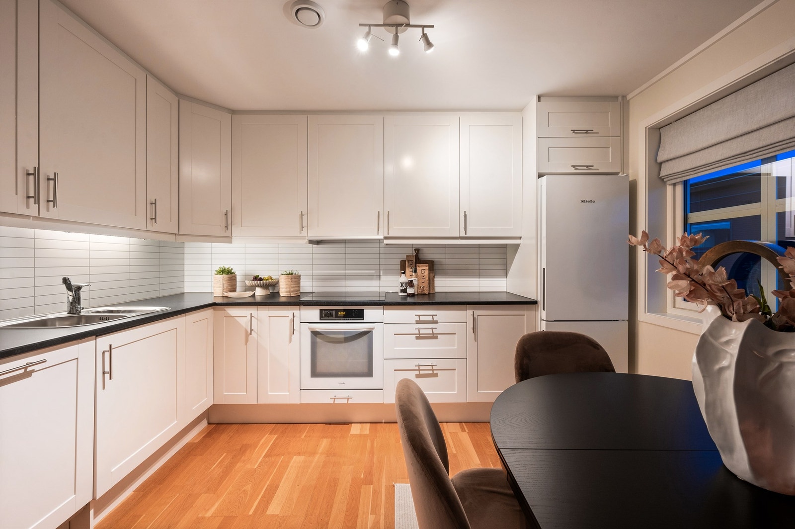 Her er kjøkkenet holdt i en sosial åpen løsning mot stuen der du har god kommunikasjon med gjestene mens middagen lages. Over benkeplaten er det splashboard og belysning. Galleribilde