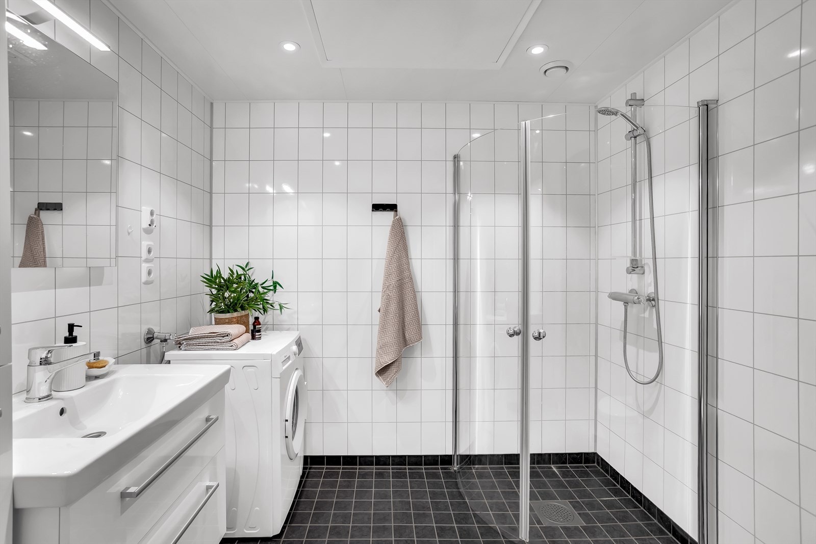 Badet er innredet med hvit servantinnredning med skuffeseksjon, høyskap, speil, toalett, dusjhjørne og opplegg for vaskemaskin. Galleribilde