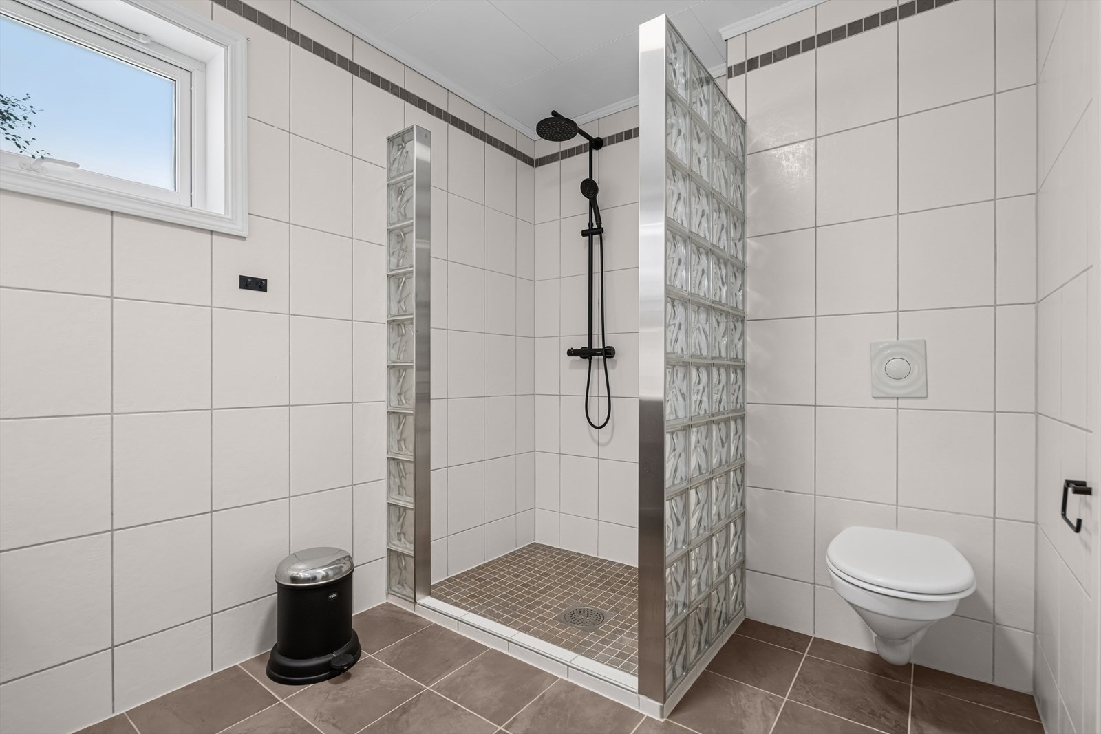 Videre finner du et vegghengt toalett som gir et moderne preg og gjør renhold enklere, samt et praktisk dusjhjørne med forheng. Ventilasjonen er løst med mekanisk avtrekk via sentralavtrekksanlegg, og tilluft kommer gjennom en spalte under døren. Galleribilde