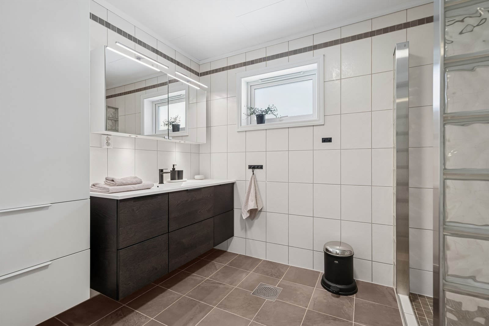 Fra hallen er det tilgang til et romslig, helfliset baderom med elektrisk gulvvarme. Innredet med Kvik-møbler, heldekkende servant, speilskap med belysning og høyskap for god oppbevaring. Galleribilde