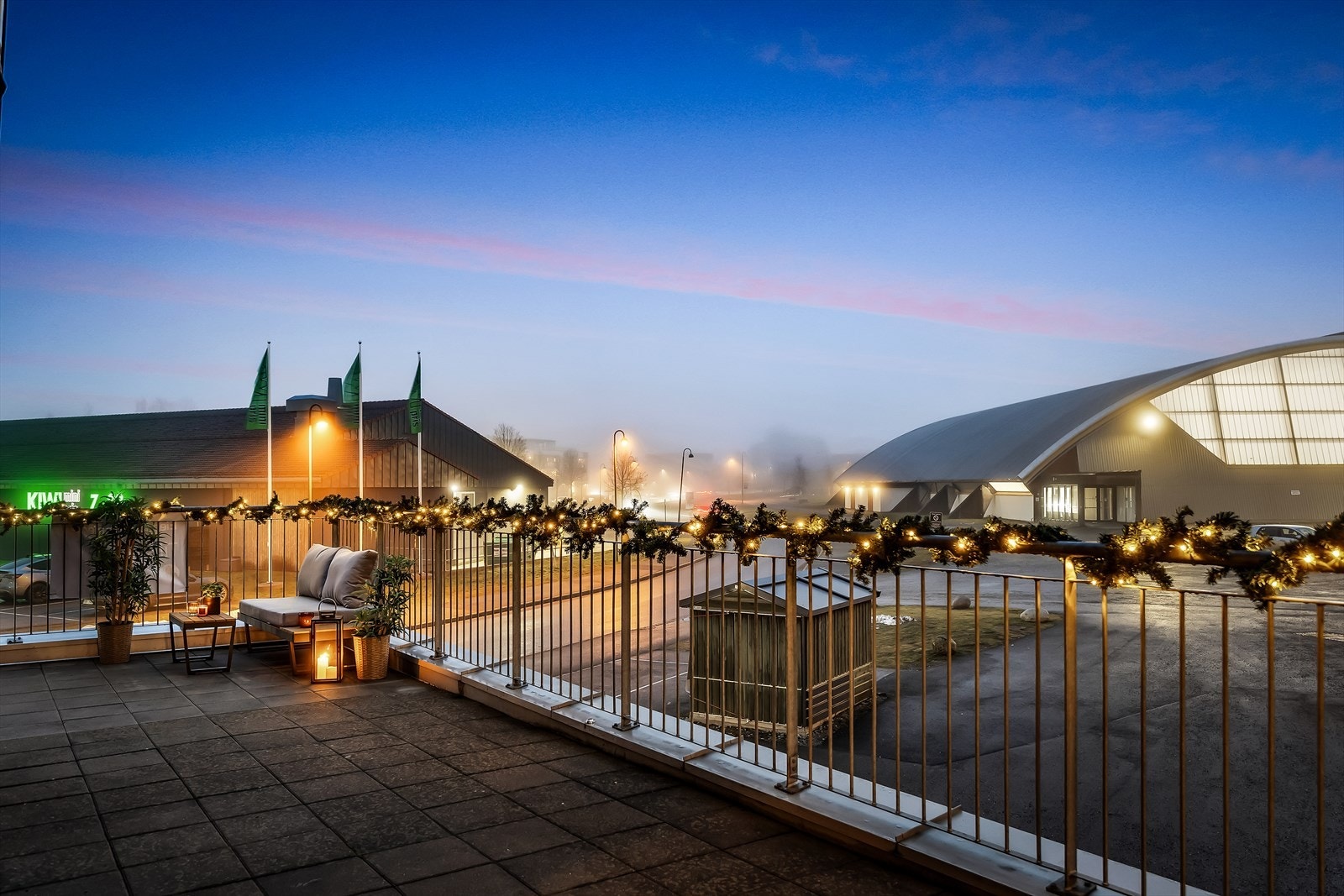 Utsikt fra sydvendt terrasse mot nærliggende Kiwi butikk og idrettsanlegg. Galleribilde