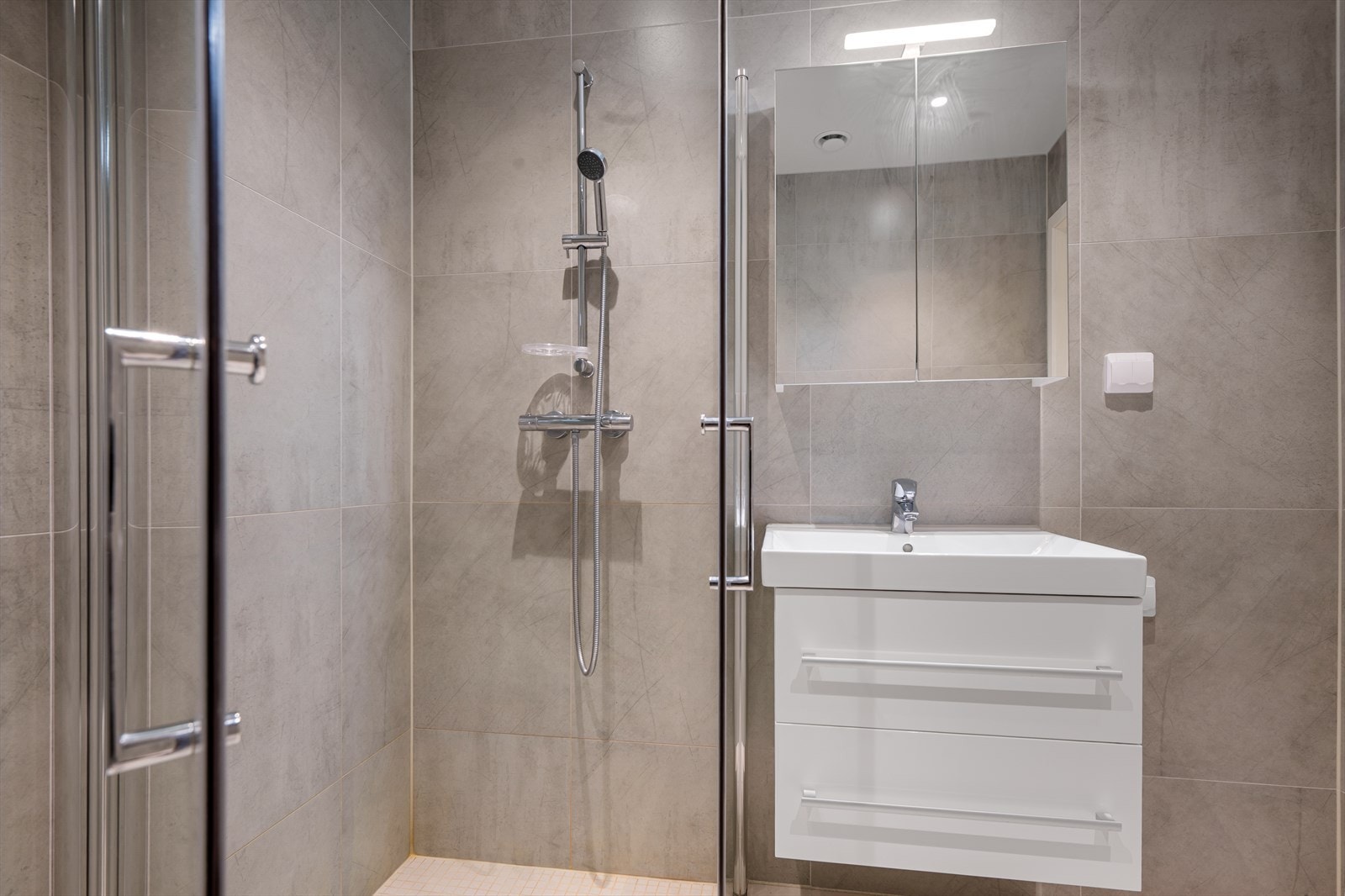 Badet er innredet med helservant på skuffeseksjon, speilskap, dusjhjørne og vegghengt toalett. Opplegg for vaskemaskin. Galleribilde