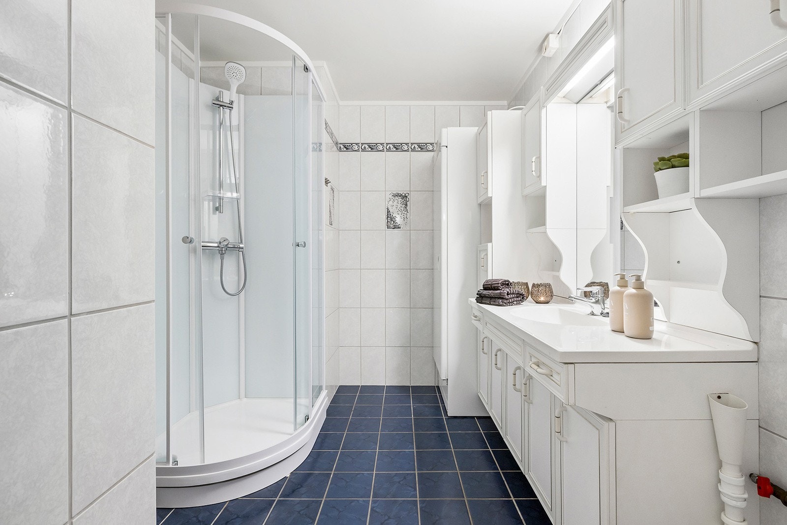 Flislagt bad med dusjkabinett, hvit baderomsinnredning og opplegg for vaskemaskin Galleribilde