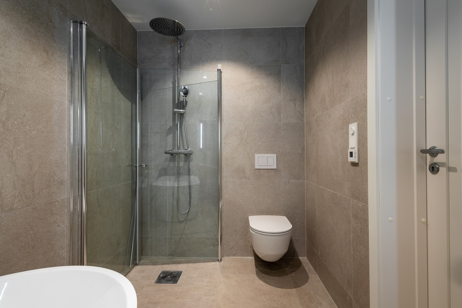 Lekkert flislagt bad med behagelig gulvvarme, dusjhjørne og badekar. Stilren servantinnredning, vegghengt toalett og speil med integrert belysning. Galleribilde