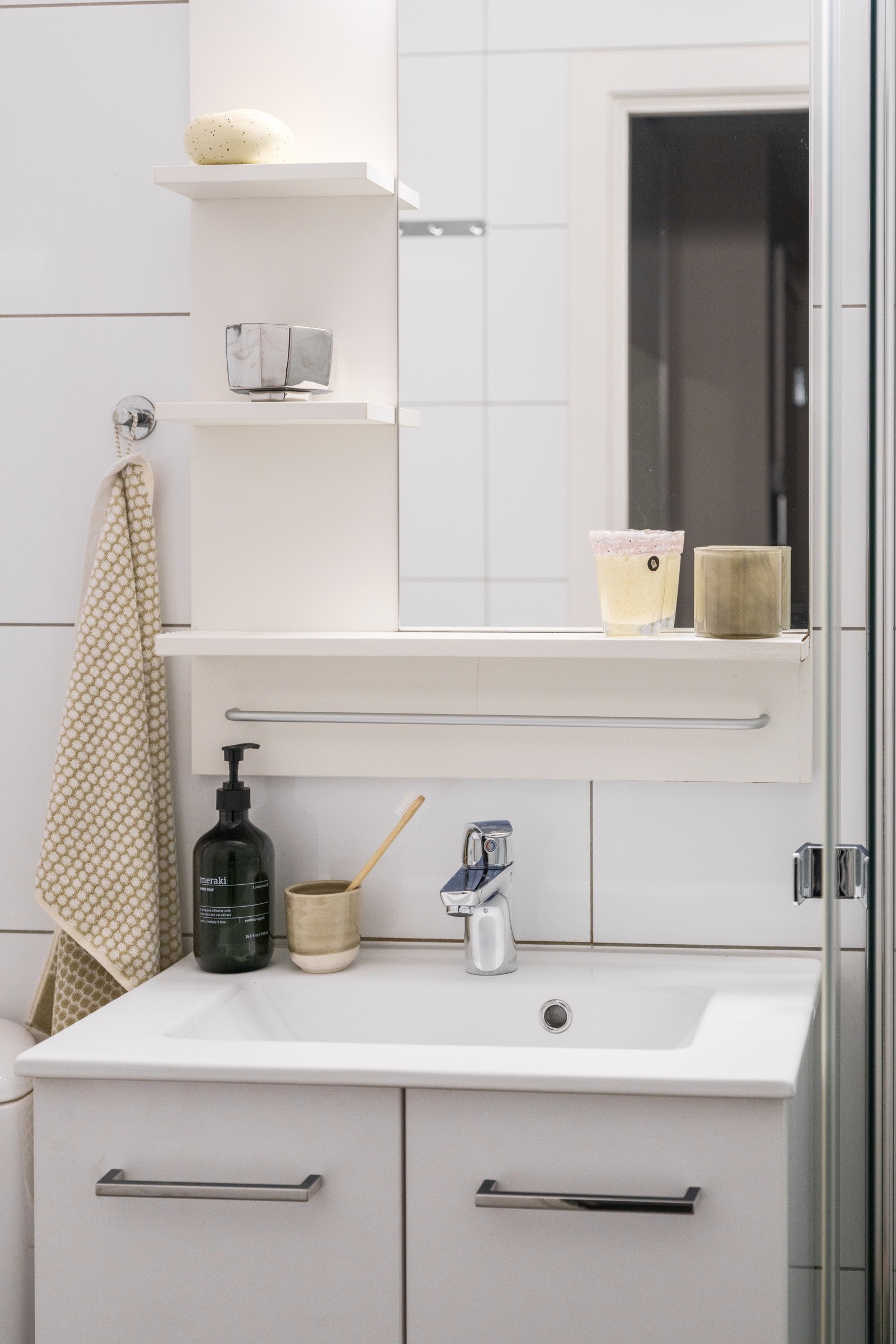 Lys baderomsinnredning med heldekkende servant, speil med hyller og belysning over. Galleribilde