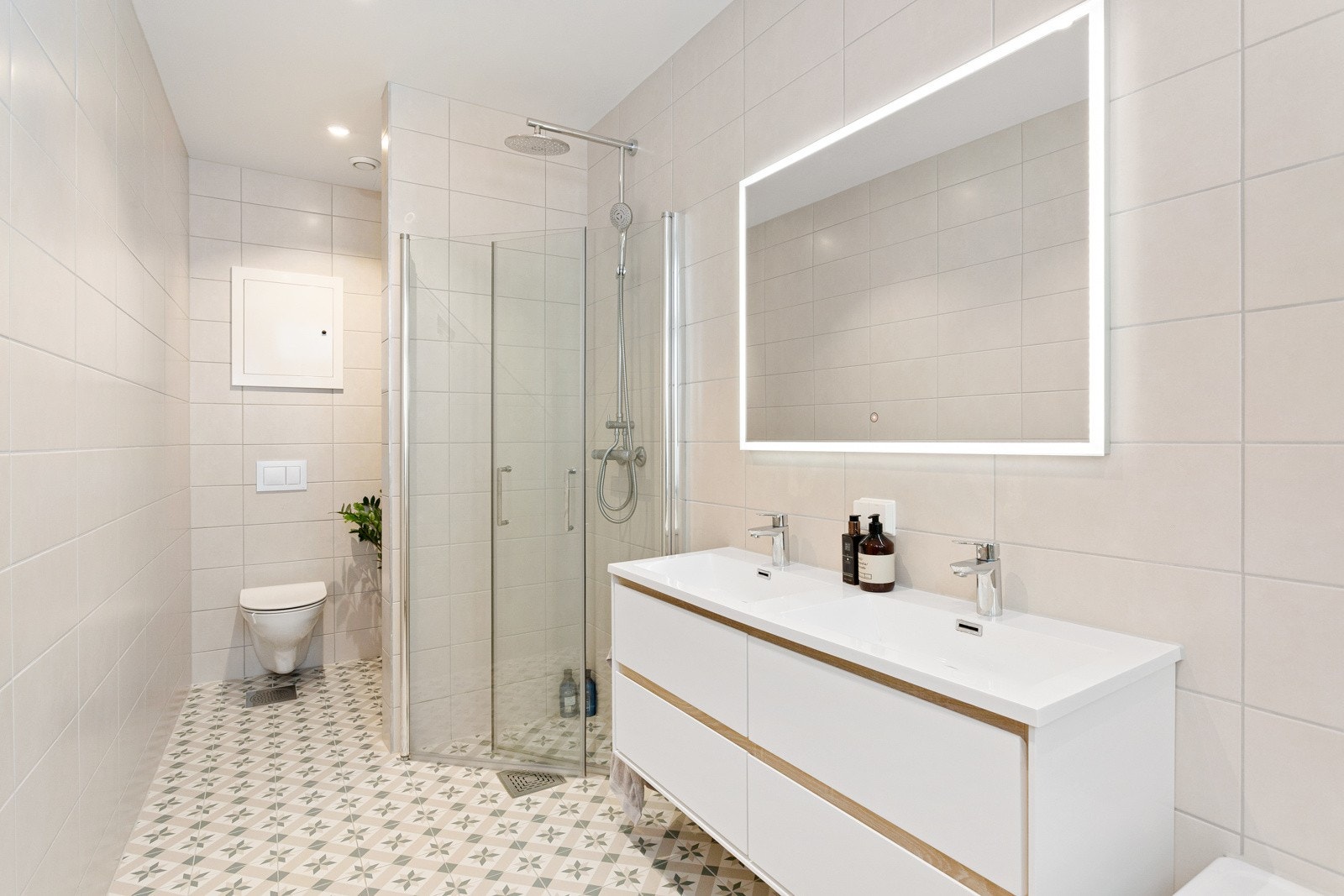 Moderne baderomsinnredning med skuffer og heldekkende dobbel servant, stort speil med integrert belysning over. Galleribilde