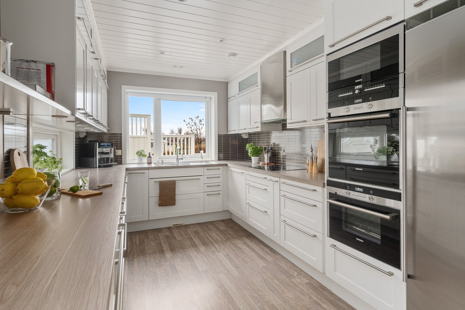 Lys kjøkkeninnredning med integrerte hvitevarer. Uttak til sentralstøvsuger ved gulv under vask. Galleribilde