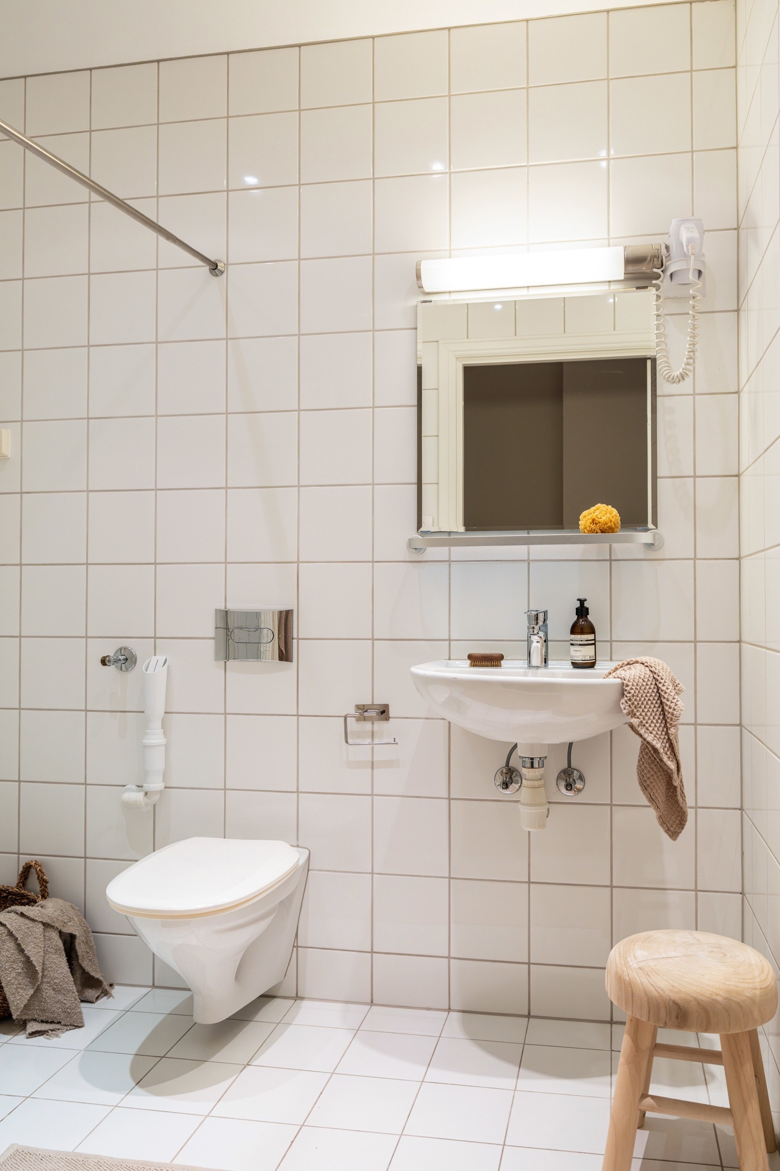 Baderommet er utstyrt med vegghengt servant, speil med hylle og belysning over, vegghengt toalett og dusjhjørne med glassdør og forheng. Galleribilde