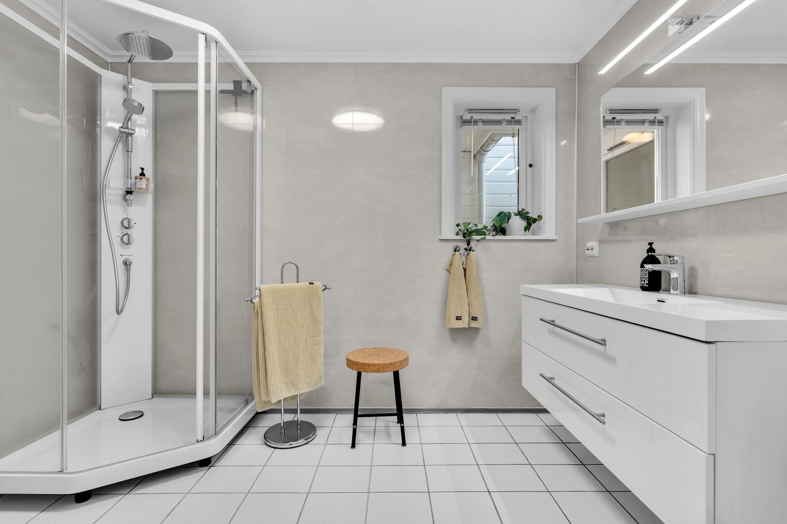 Stilrent bad med fliser på gulvet, dusjkabinett, toalett og baderomsinnredning med oppbevaringsmuligheter. Galleribilde