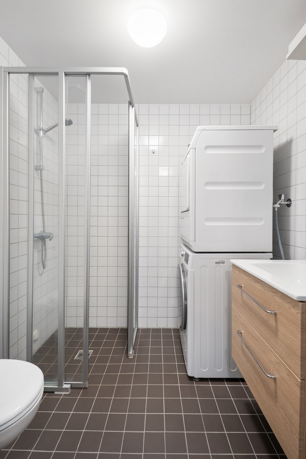 Rommet er innredet med dusjhjørne med skjermvegger og skyvedør, vegghengt klosett, hel nedfelt servant, baderomsinnredning med servantskap og opplegg for vaskemaskin og tørketrommel. Galleribilde