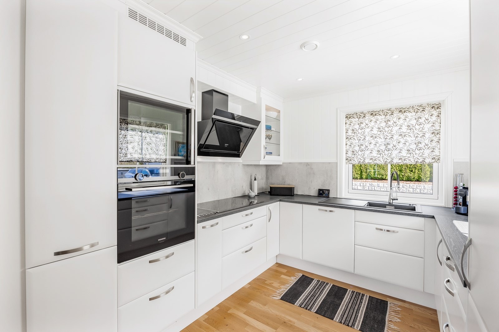 Stilren kjøkkeninnredning med hvite, glatte fronter og laminert benkeplate. Galleribilde