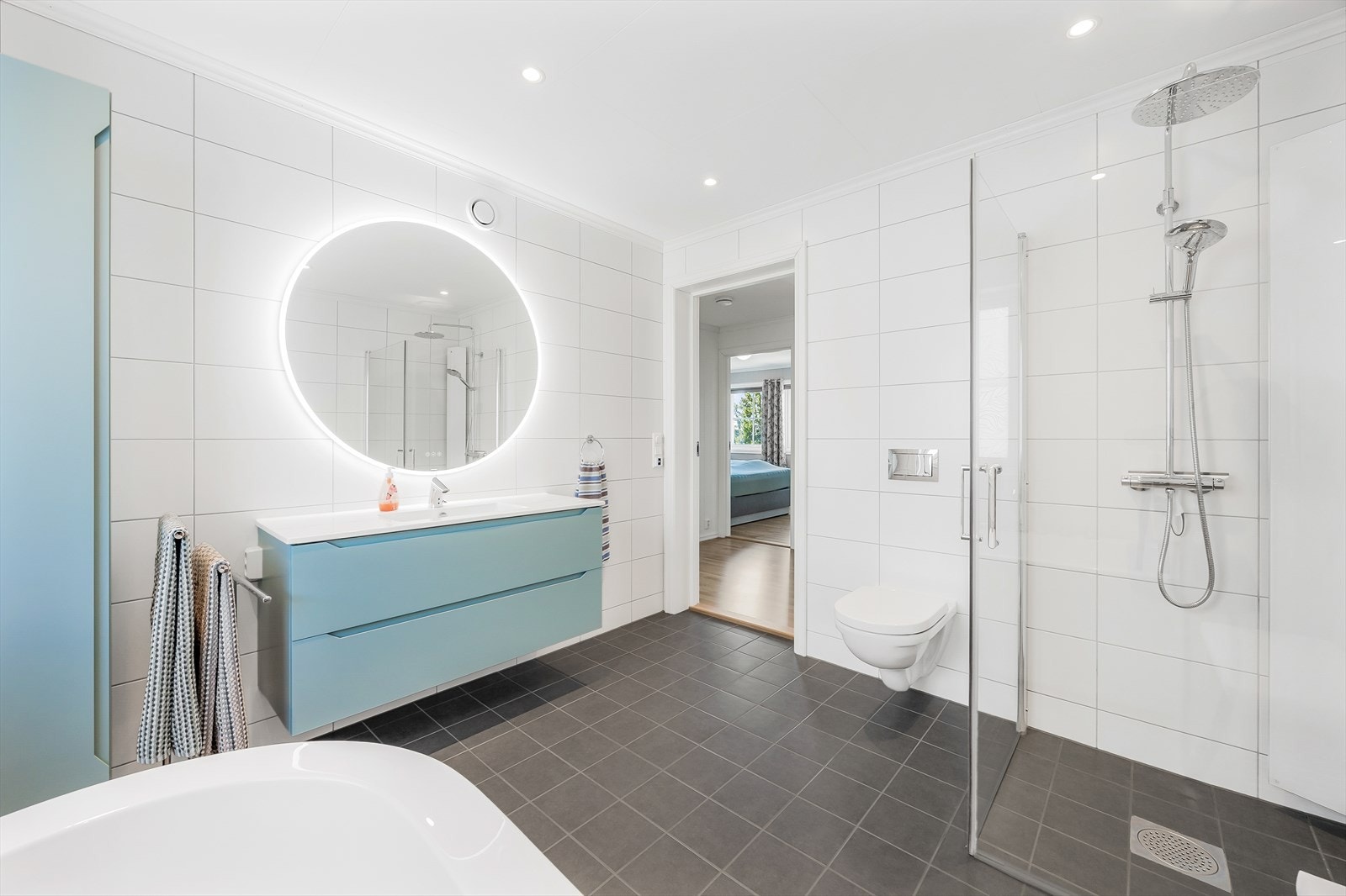 Badet er innredet med servant i baderomsinnredning, vegghengt hjørneskap, badekar, vegghengt toalett og dusjhjørne. Galleribilde