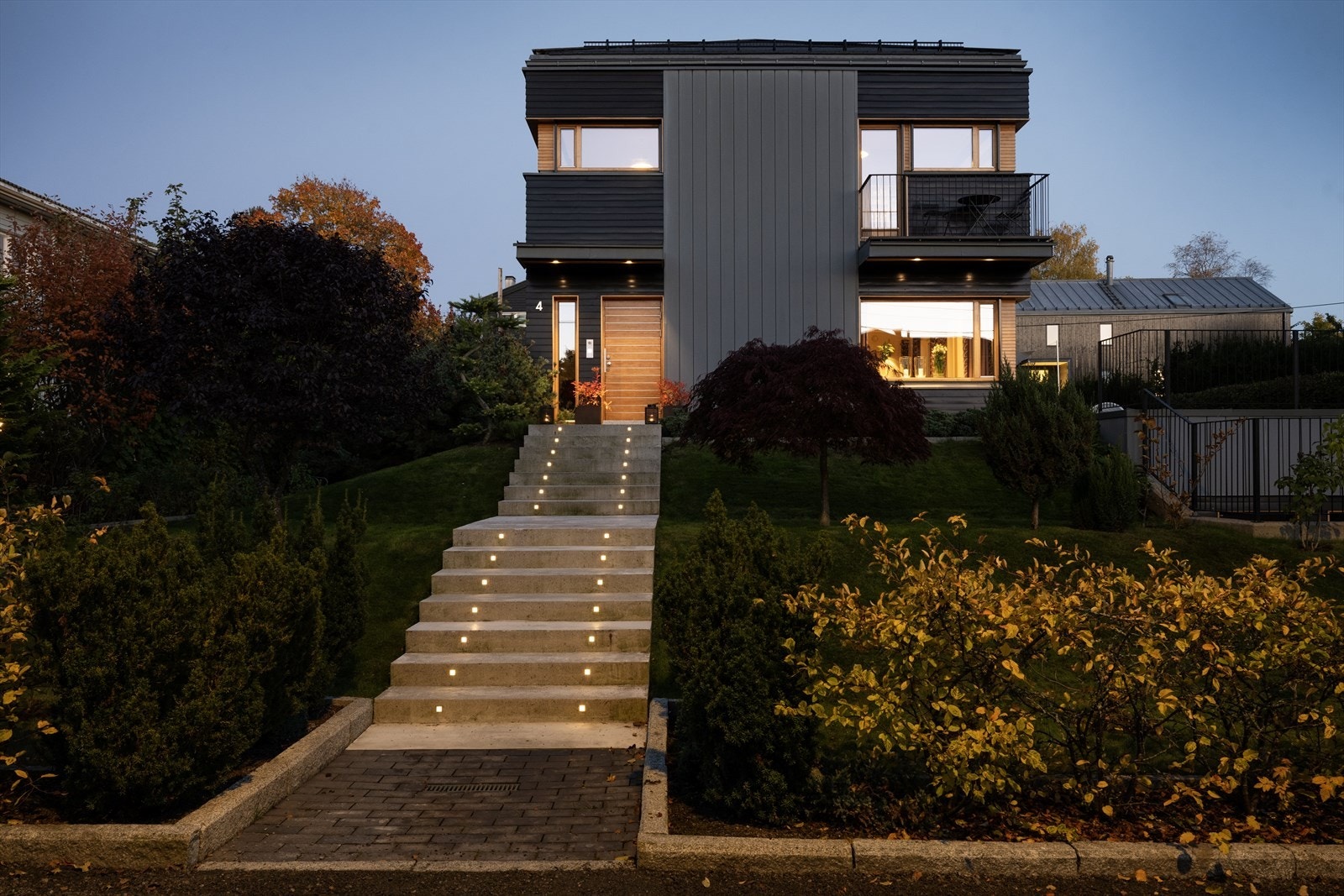 Representativt inngangsparti med trapper av betong med varmekabler som er anlagt inn i terrenget. Solid ytterdør av eik og Gira ringesystem med video og åpningsmulighet i alle etasjer. Galleribilde