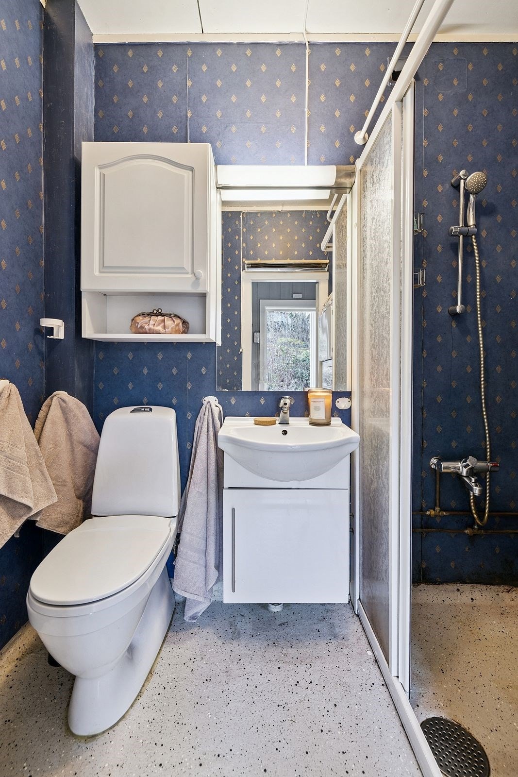 Badet er innredet med gulvstående toalett, vegg hengt servantinnredning med skapdør og spel med overlys og stikkontakt over servant Galleribilde