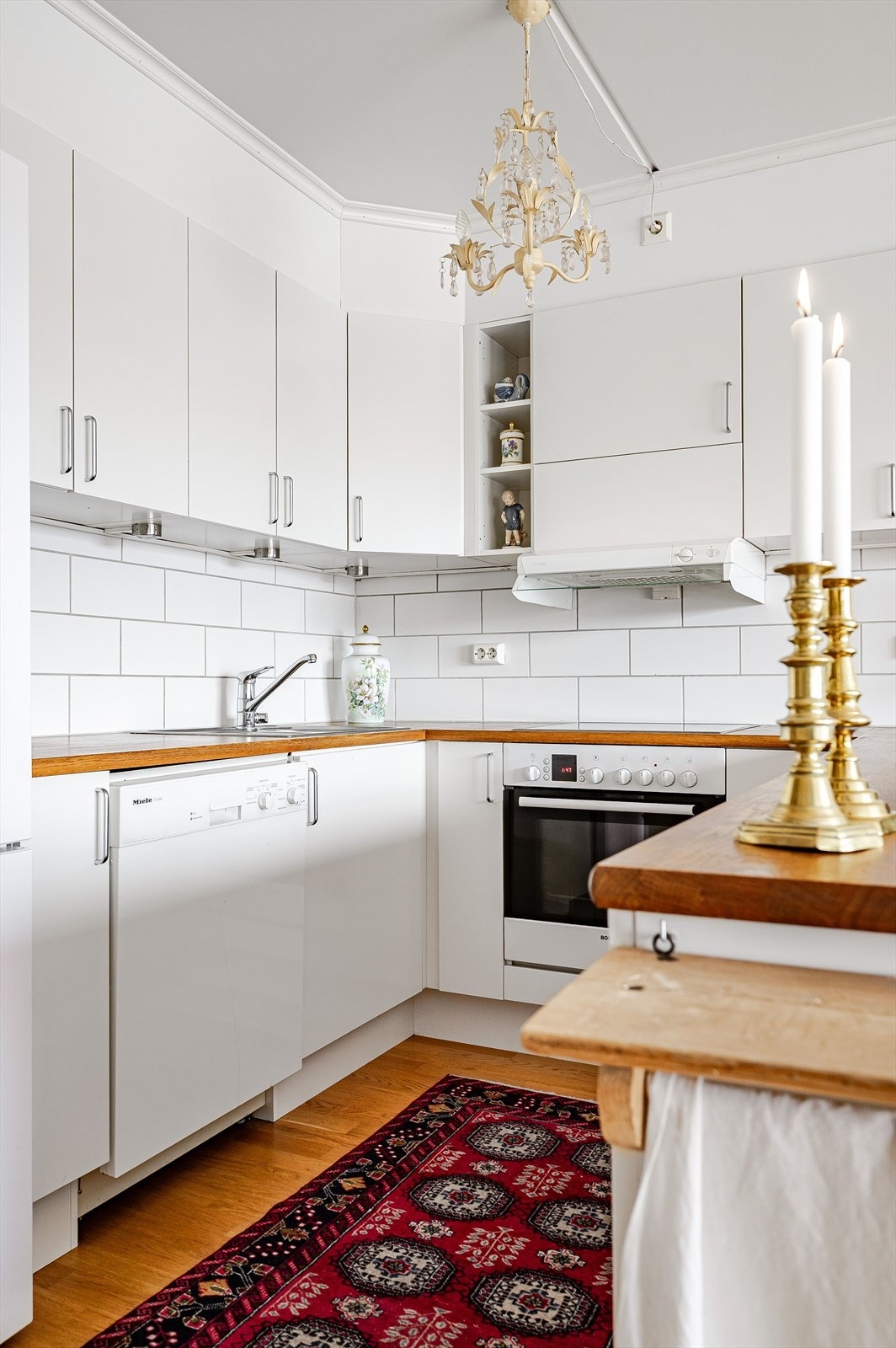 Lys og tidløs kjøkkeninnredning med hvite glatte fronter og heltre benkeplate med nedfelt oppvaskkum. Praktisk med fliser i benkeryggen og belysning under overskapene. Galleribilde