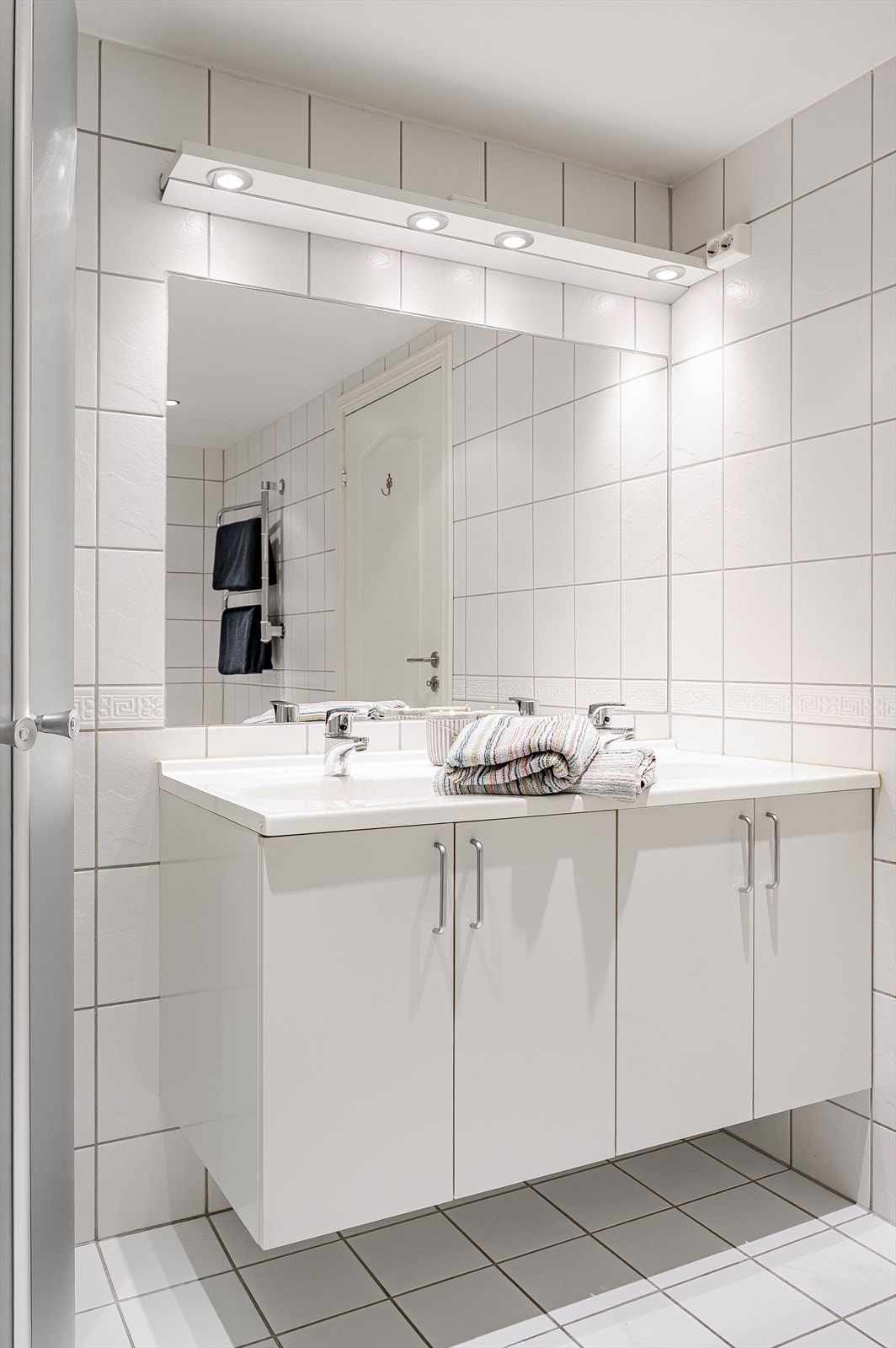 Lys baderomsinnredning med heldekkende dobbel servant, store speil med belysning over. Galleribilde