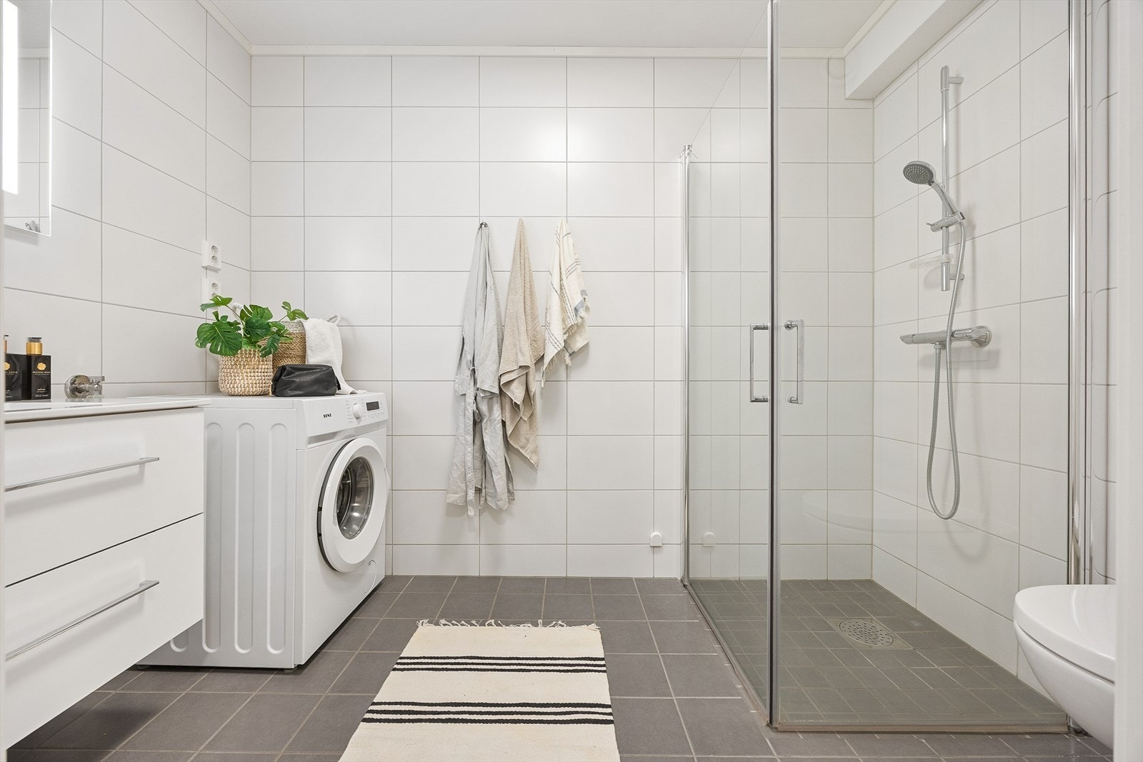 Moderne, flislagt bad fra 2023 med keramiske fliser på gulv og vegger, samt opplegg for vaskemaskin. Galleribilde