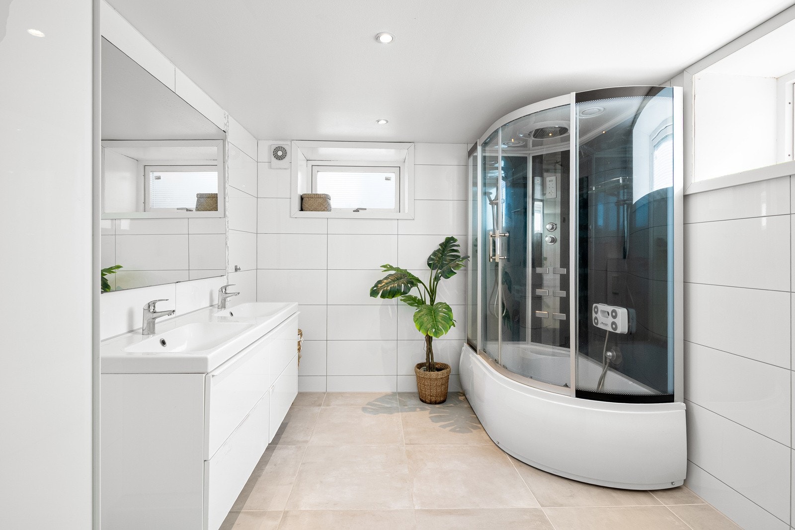 Badet i kjelleren fremstår moderne og innbydende, med fliser på både gulv og vegger samt malt gipstak og integrerte downlights som gir et behagelig lys. Galleribilde