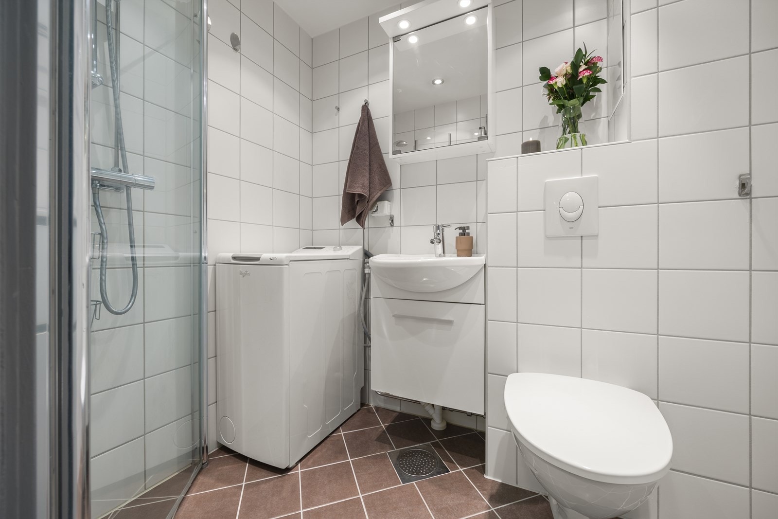 Speilskap over servant og hvit servant i helstøpt plate. Rommet har dusj på gulv med dører i herdet glass, vegghengt klosett. Galleribilde