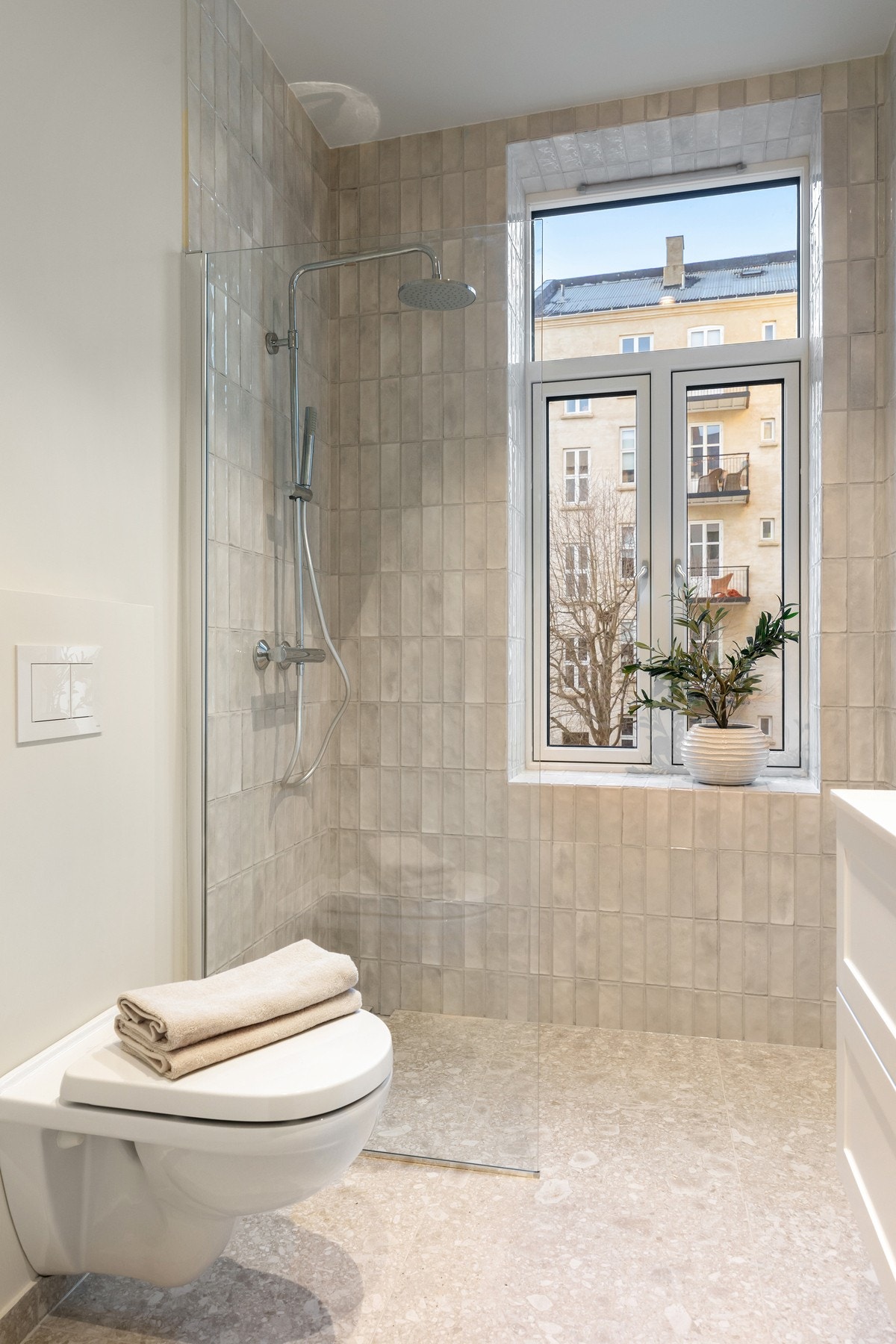 Badet er innredet med veggmontert toalett med innbygget sisterne, nedfelt servant og dusjnisje med glassdør. Galleribilde