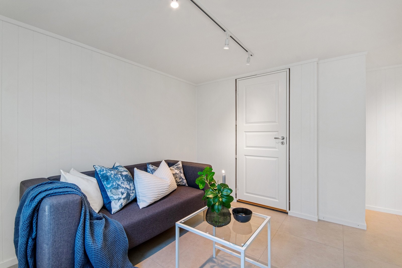 Kjellerstue med flislagt gulv og hvitmalte overflater samt lysskinne i tak som gir godt med lys. Galleribilde