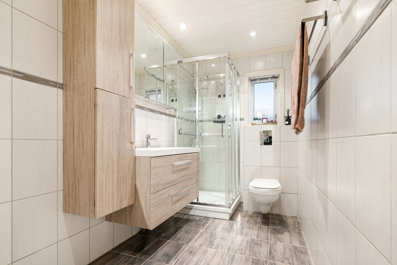 Pent flislagt baderom som har innredning med glatte fronter og porselenservant. Galleribilde