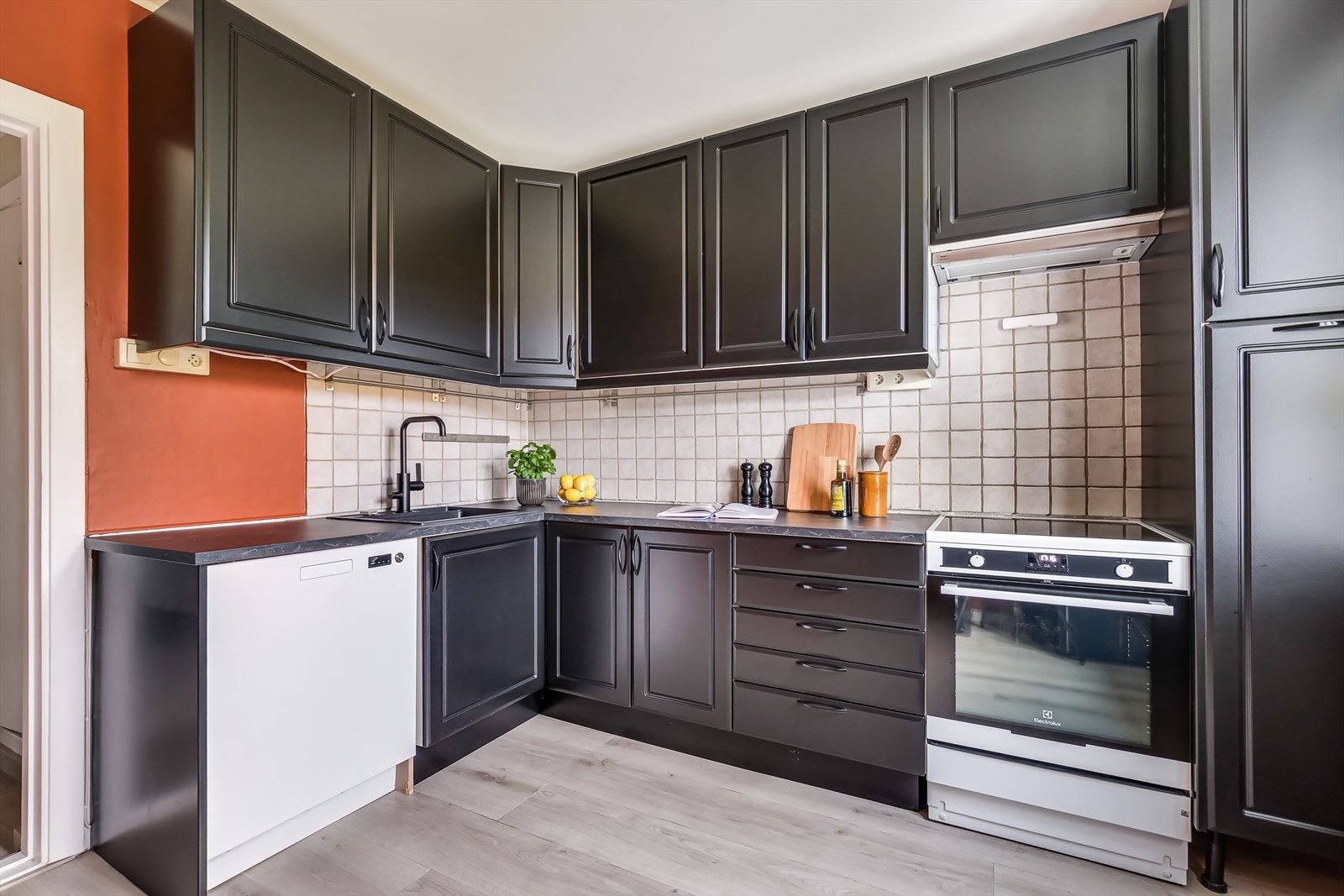 Kjøkkeninnredning med svarte profilerte fronter, laminert benkeplate og fliser over benk. Det er belysning under overskap som gir godt arbeidslys. Galleribilde