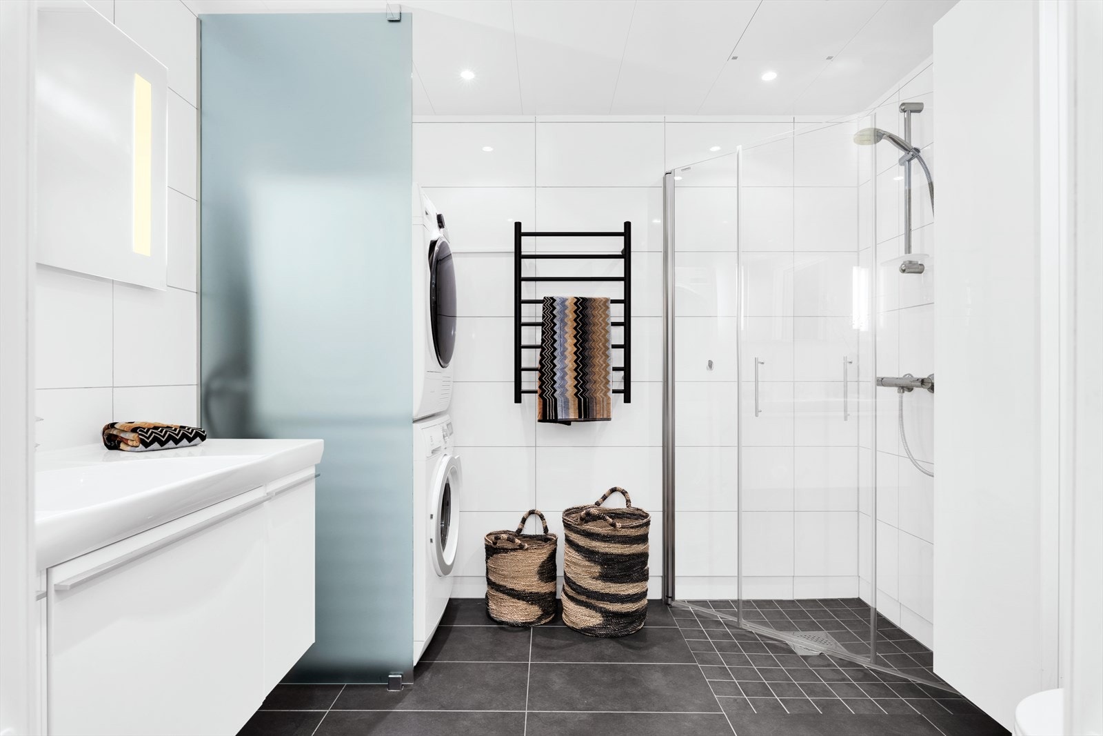 Badet er innredet med hvit baderomsinnredning, speil, dusjhjørne og vegghengt toalett Galleribilde