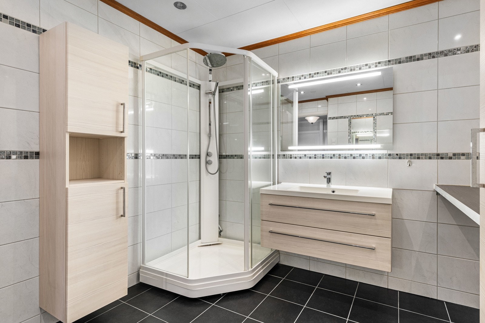 Badet er innredet med toalett, servant, speil med integrert belysning og dusjkabinett. Galleribilde