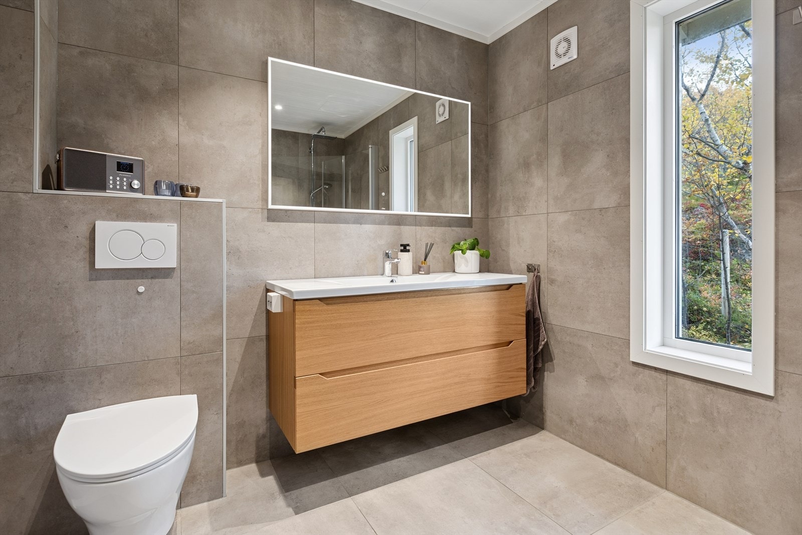 Badet er utstyrt med blant annet gulvvarme, vegghengt toalett, regnfallsdusj med innfellbare dusjdører og speil med integrert belysning. Galleribilde