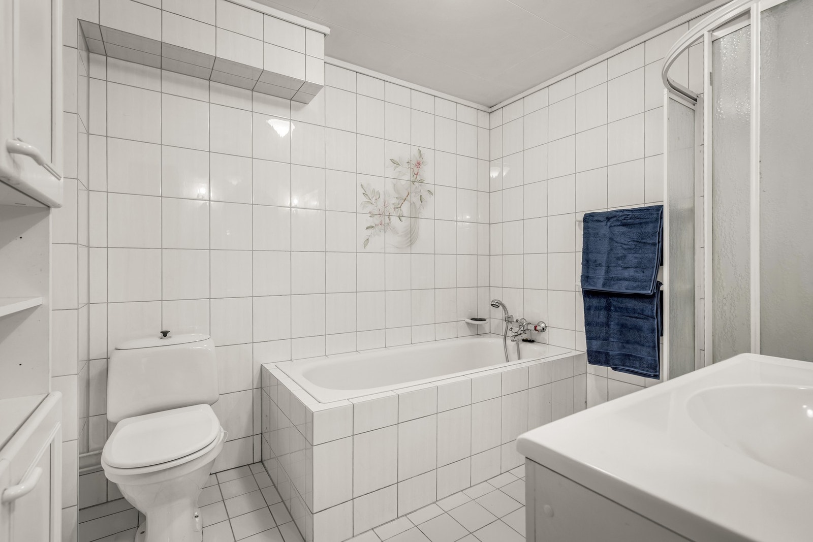 Badet er av eldre dato og består av servant med underskap, badekar, dusjkabinett og toalett. Galleribilde