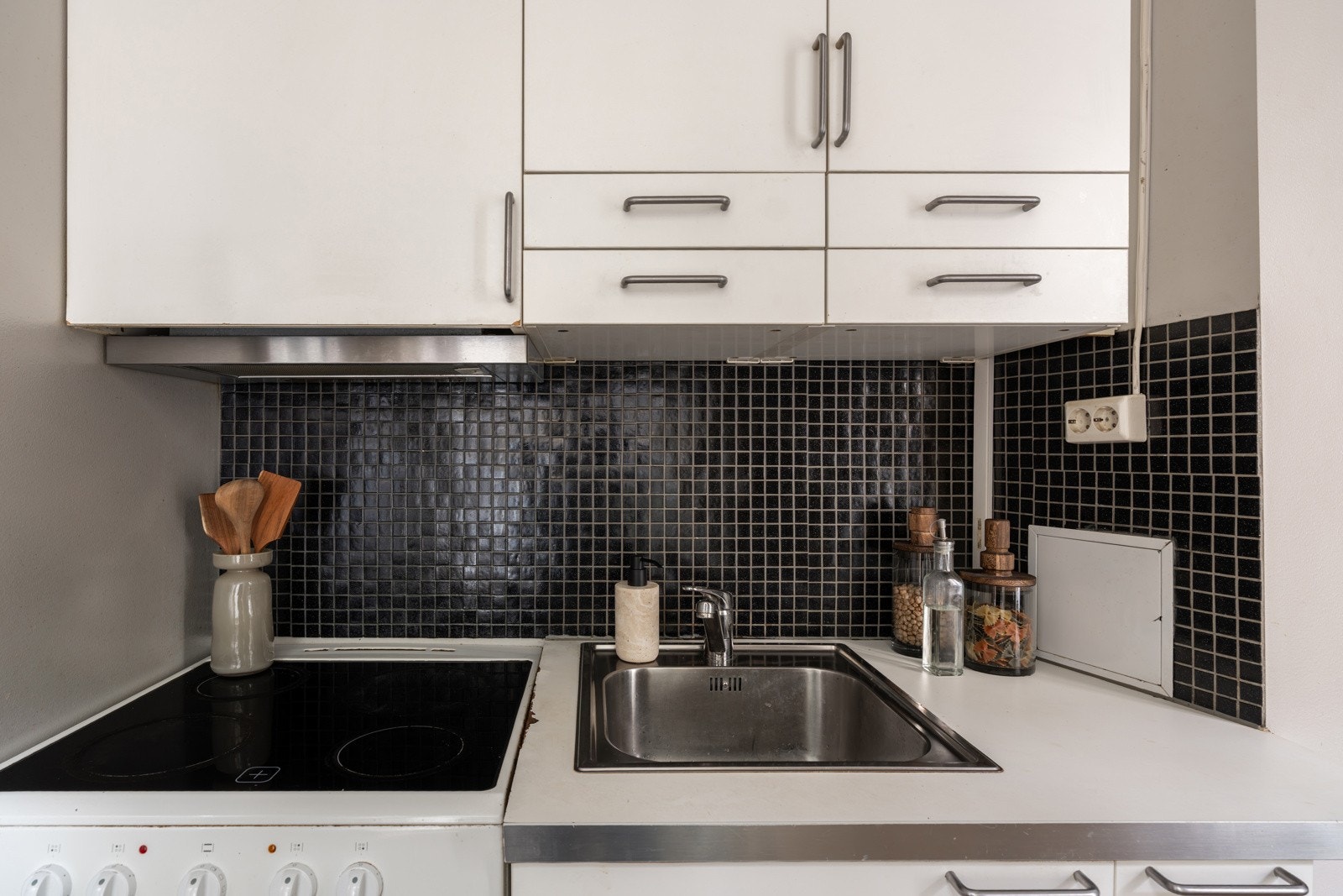 Enkel kjøkkeninnredning med hvite glatte fronter og laminert benkeplate med nedfelt oppvaskkum. Praktisk med mosaikkfliser i benkeryggen. Galleribilde