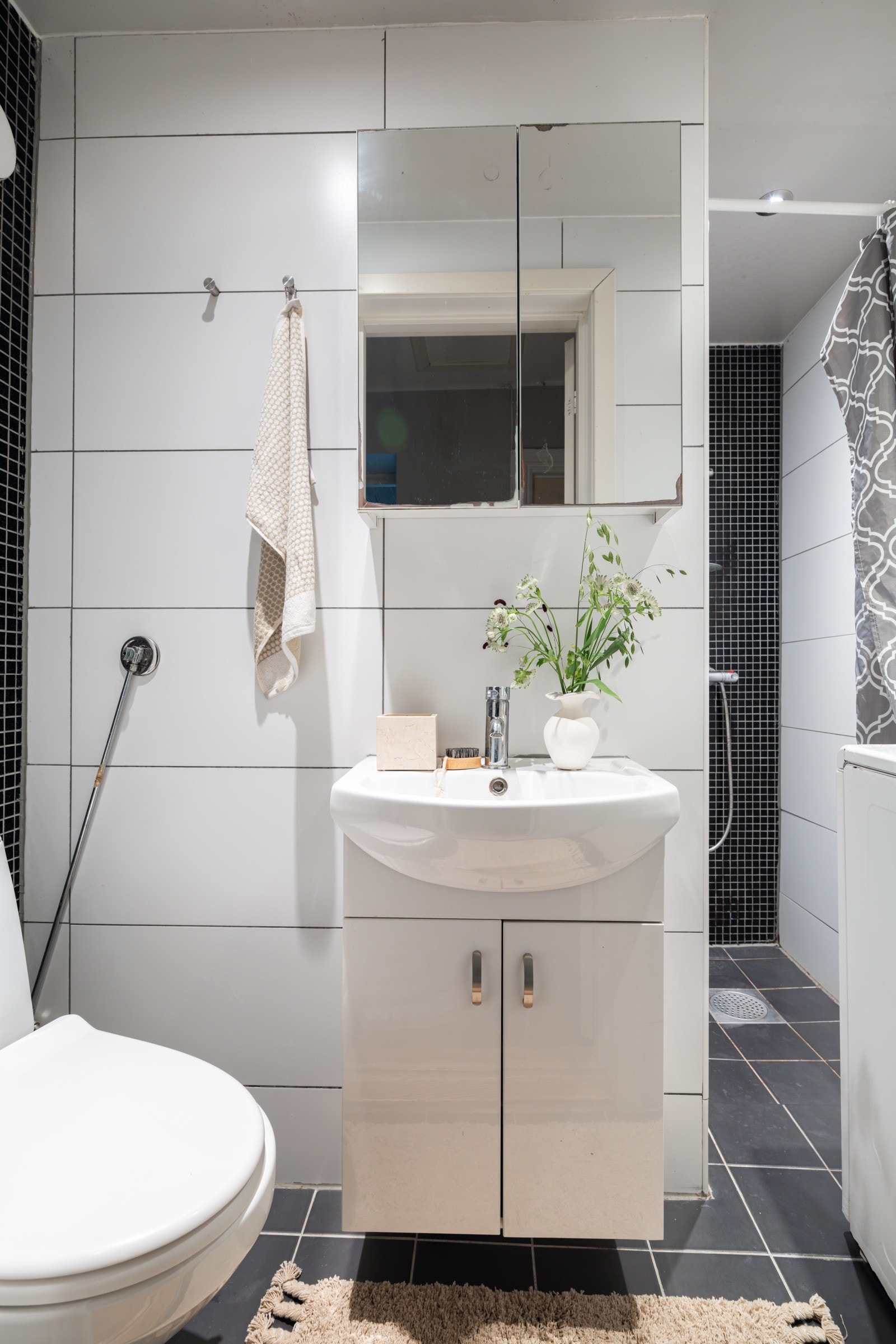 Leiligheten har et flislagt baderom fra ukjent årstall. Baderommet har mørke fliser på gulv, hvite fliser kombinert med sorte mosaikkfliser på veggene og downligths i himlingen. Galleribilde