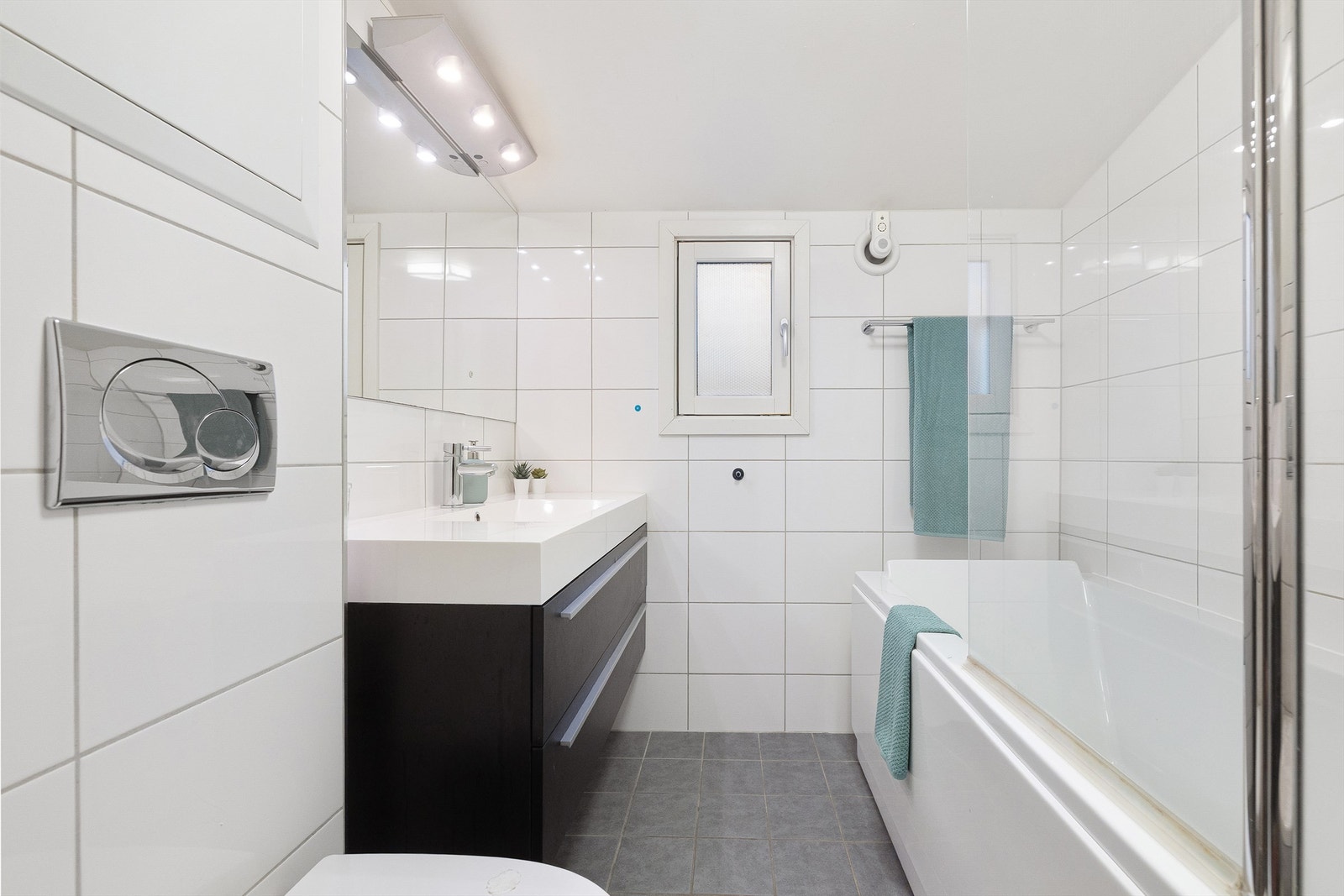 Badet ble oppgradert i 2012 og har hvite fliser på veggene og grå fliser på gulvet. Det er innredet med heldekkende servant med stort speil, vegghengt toalett og badekar - perfekt for avslapning. Varmekabler i gulvet gir ekstra komfort. Galleribilde