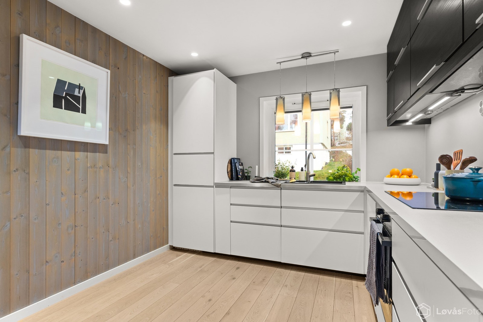 Tidløst kjøkken hvor deler av veggen har panel, noe som deler opp og gir varme i det store oppholdsrommet. Galleribilde