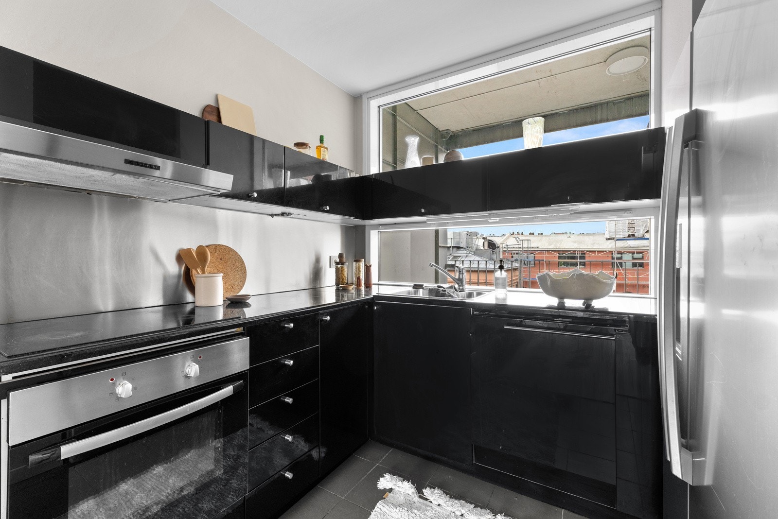 Pen kjøkkeninnredning med stålplate og belysning over benkeplate i stein med oppvaskkum og 1-greps blandebatteri. Galleribilde