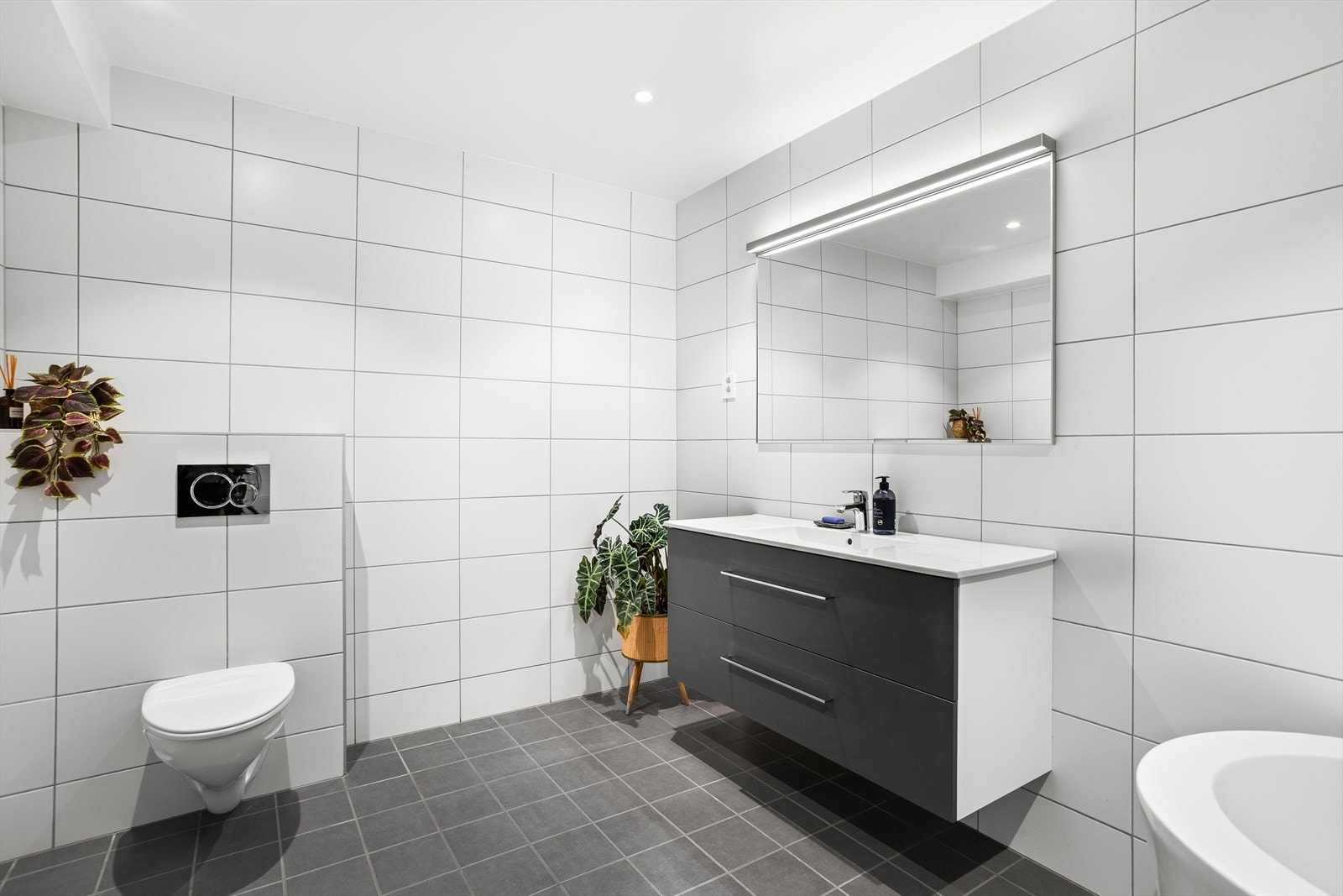 Badet er innredet med servantskap med en overliggende servant, speil, toalett, frittstående badekar og dusjhjørne. Galleribilde