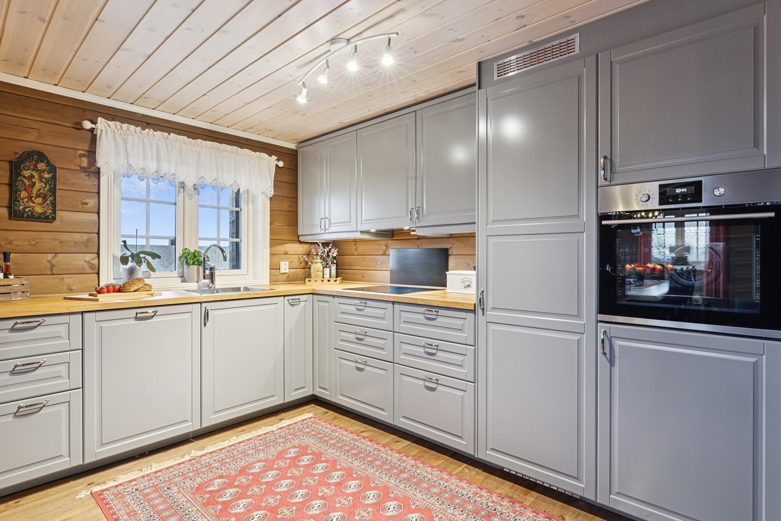 Grå profilerte fronter, benkeplate i heltre og vaskekum. Integrerte hvitevarer. Galleribilde