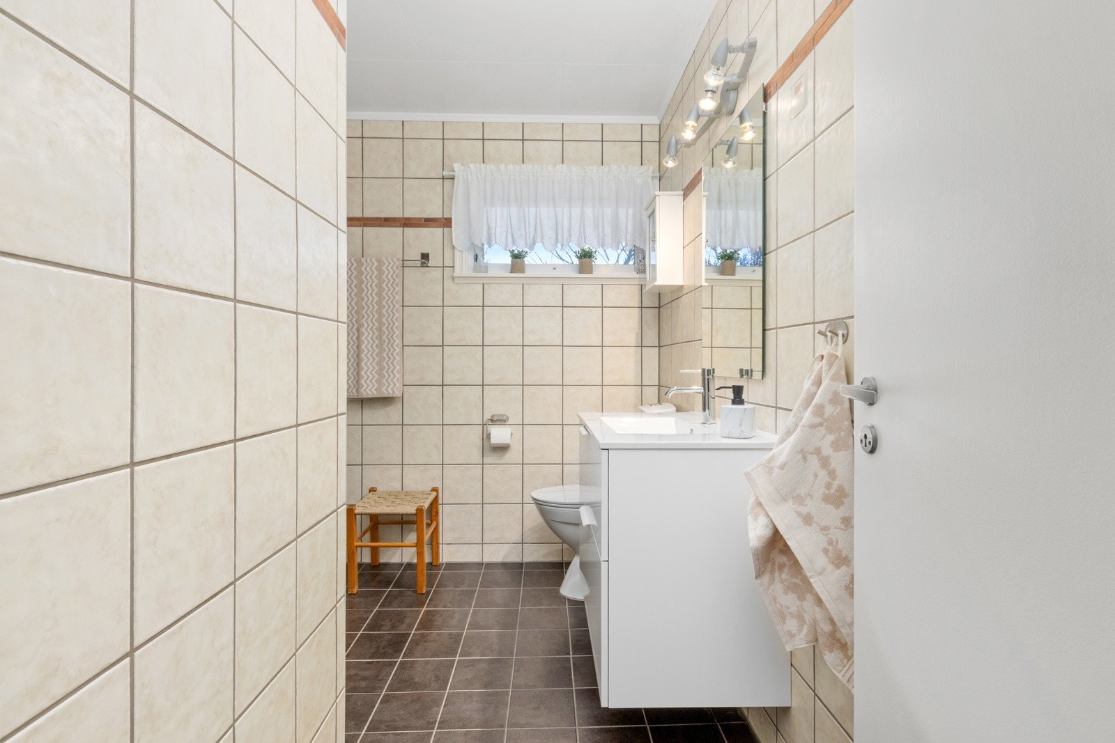 Flislagt bad med varmekabler i gulv, klosett, dusjhjørne og servant med skap. Galleribilde