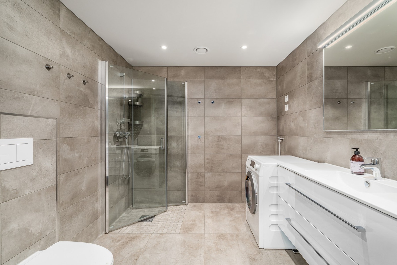 Stilrent baderom utstyrt med elektriske varmekabler i gulv og opplegg for vaskemaskin. Galleribilde