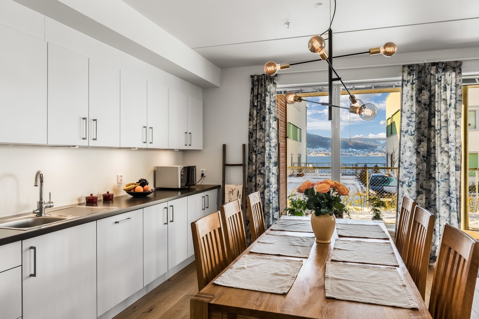 Den laminerte benkeplaten inkluderer en praktisk nedfelt vask, og kjøkkenet er utstyrt med integrerte hvitevarer som oppvaskmaskin, kjøl/fryseskap og komfyr med platetopp, noe som gir en enhetlig stil og effektiv bruk av plassen. Galleribilde