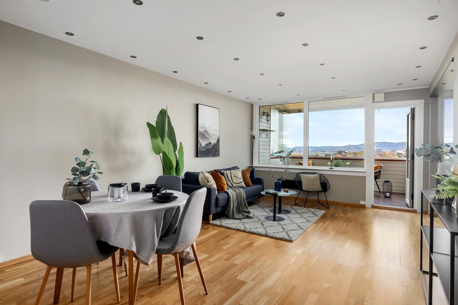 Lys stue med åpen løsning mot kjøkken, store vindusflater og utgang til innglasset balkong. Galleribilde