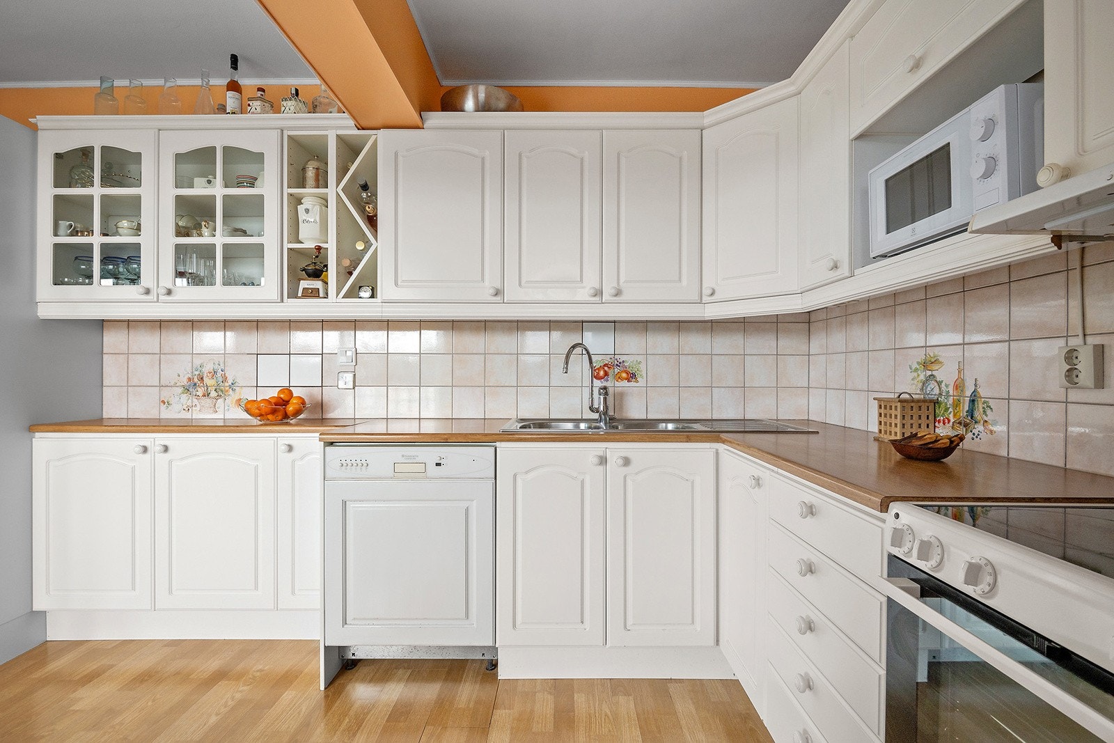 Kjøkkeninnredning med et-speils fabrikklakkerte skapfronter, laminat benkeplate med fliser på bakvegg, dobbel oppvaskkum og ventilator. Galleribilde