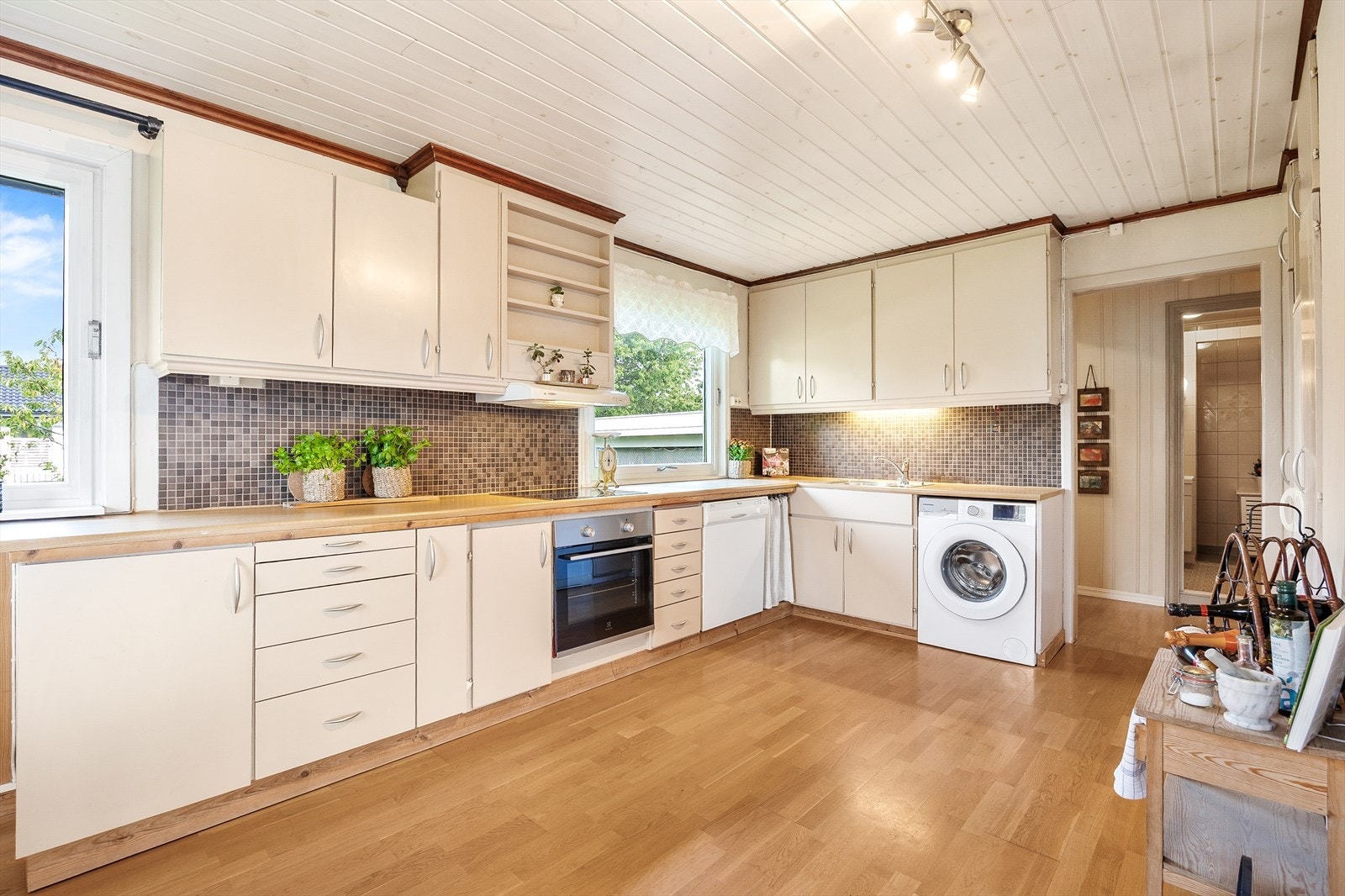 Innredningen har beige, glatte fronter og dobbel oppvaskkum nedfelt i benken. Videre er stekeovn og induksjonstopp integrert, og det er opplegg for oppvaskmaskin og vaskemaskin under benken. Galleribilde